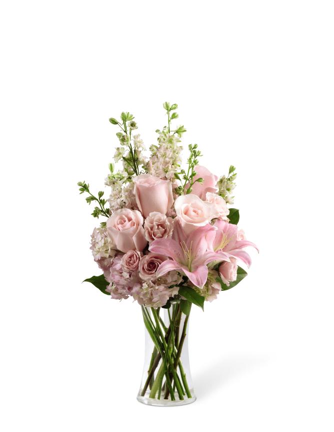 Tall arrangement of soft pink roses and lilies with white accents in a clear glass vase