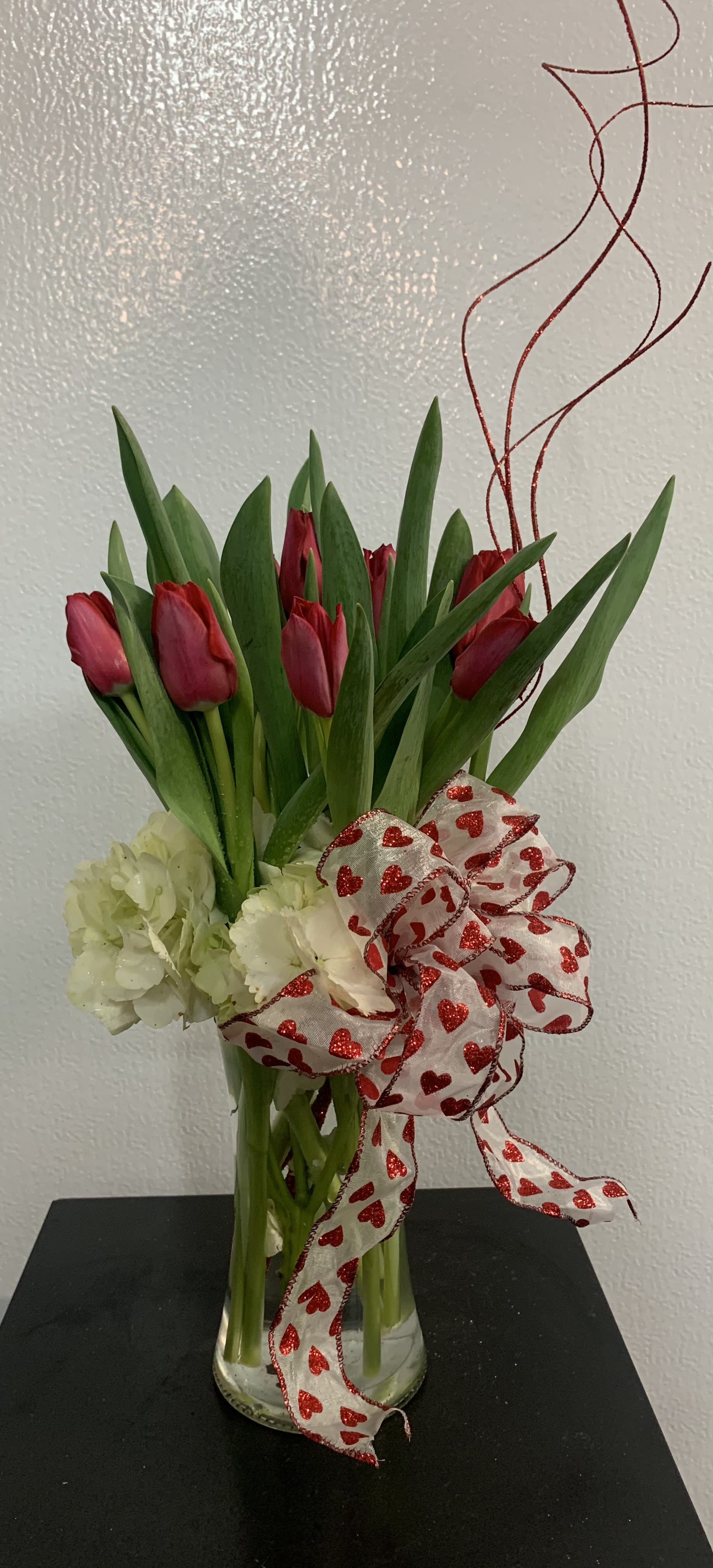 Radiantly Red Tulip Bouquet - Beautiful and "simply said" red tulips are a hip way to show you care.    Ten romantic red Tulips with a base of white hydrangea arranged in a clear glass vase.  Ribbon will vary depending on season  Approximately 12" W x 14" H  