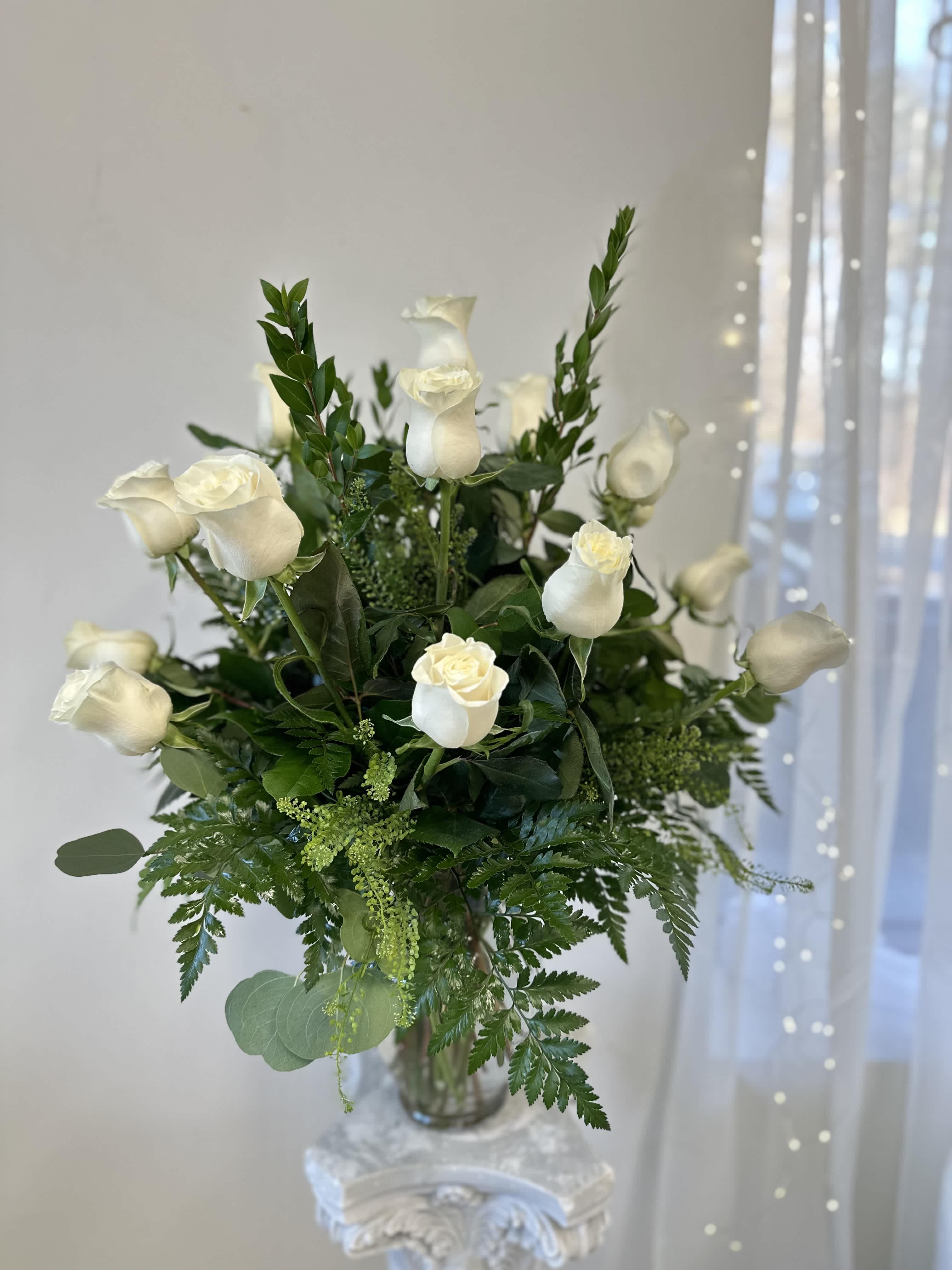 Dozen White Roses by Westford Florist Art by Veny - The sight of a dozen white roses by Westford Florist Art by Veny elegantly arranged in a tall glass vase is truly breathtaking. This classic and sophisticated floral arrangement exudes a sense of peace and purity, making it the perfect gift for any occasion. The pure white petals against the sleek glass vase create a stunning visual contrast that is sure to capture anyone's attention. Whether you are celebrating an anniversary, expressing sympathy, or simply want to brighten someone's day, these white roses speak volumes without saying a word. Their timeless beauty and elegance make them a versatile choice that will never go out of style. Imagine walking into a room and being greeted by the delicate fragrance and graceful presence of these twelve white roses. It's like bringing nature indoors in the most elegant way possible. So, if you're looking for a gift that will leave a lasting impression, look no further than this stunning arrangement from Westford Florist Art by Veny.
