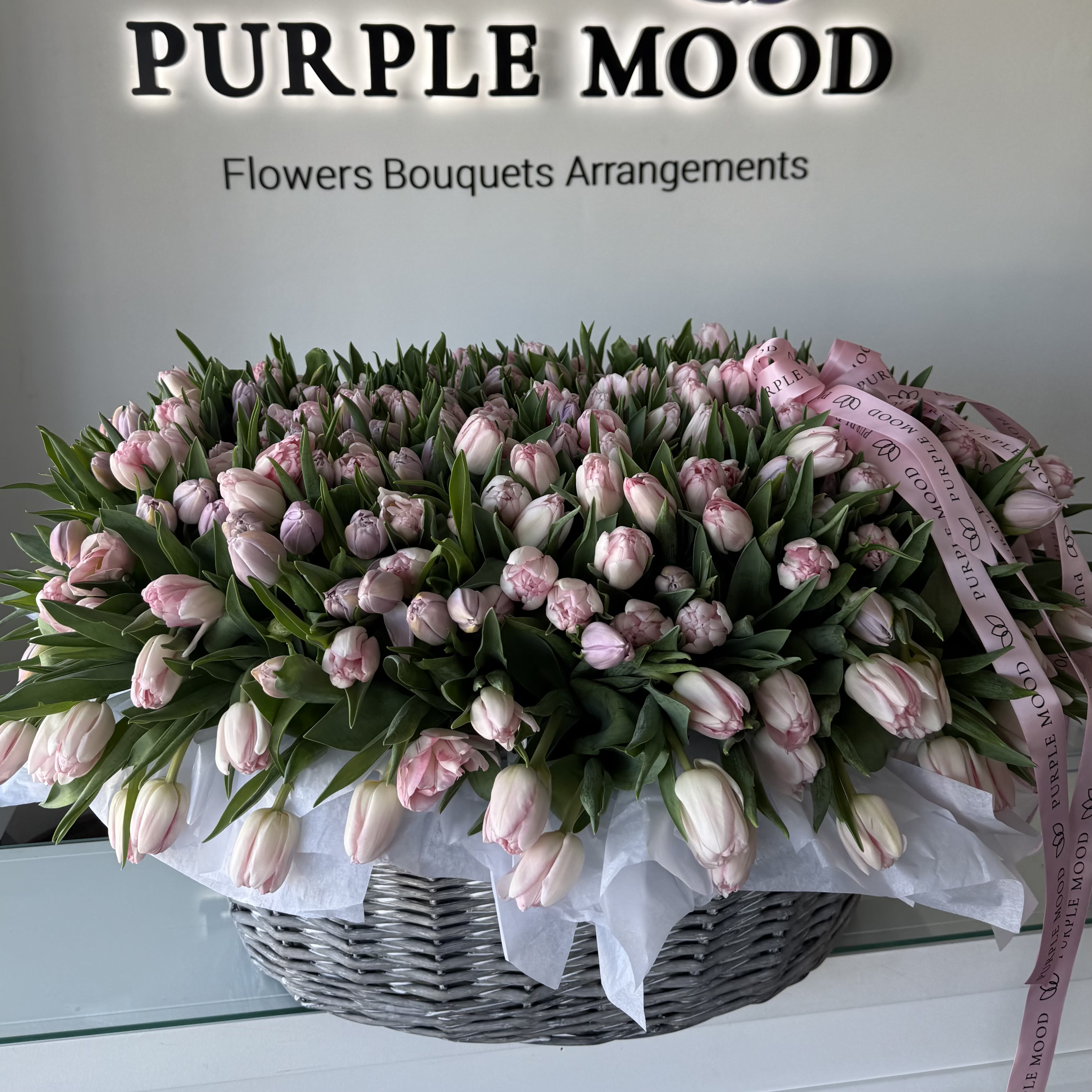 200 Pastel Tulips Basket - A breathtaking grand basket filled with 200 premium pastel tulips, hand-arranged in soft shades of blush, ivory, light pink and delicate peach.  Designed as a lush romantic floral cloud and finished with our signature Purple Mood ribbon, this elegant arrangement is perfect for Valentine’s Day, anniversaries, and unforgettable moments of love.  Please note: tulip colors may vary slightly depending on availability, but will always remain within a soft pastel palette to preserve the gentle, romantic look of this design.
