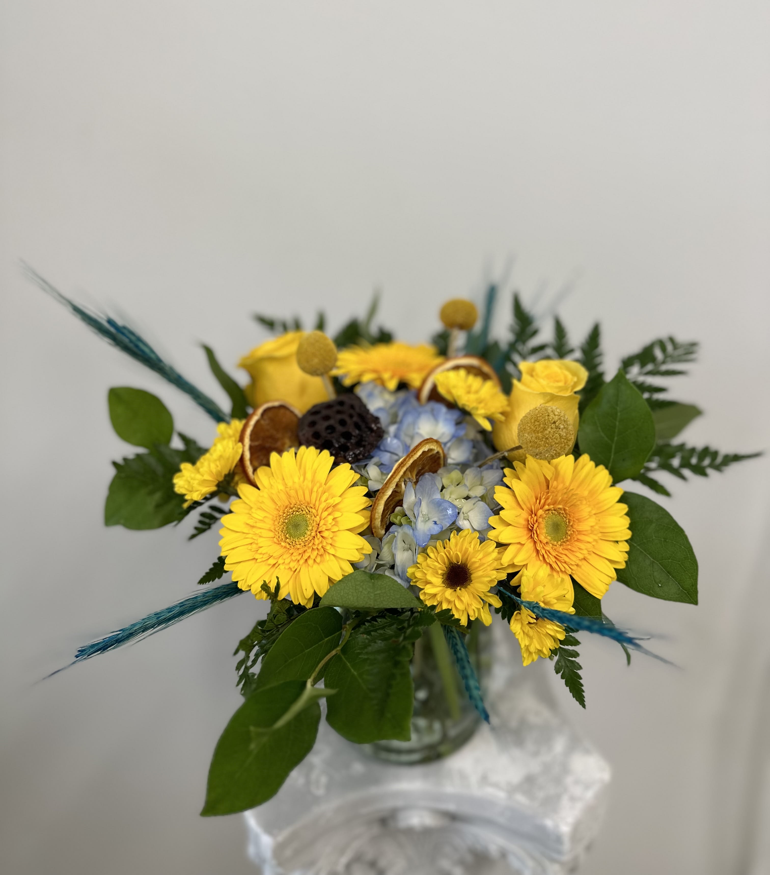 Feeling Happy by Westford Florist Art by Veny - Brighten up any occasion with our beautiful Feeling Happy by Westford Florist Art by Veny. This stunning arrangement features cheerful yellow Gerbera daisies, yellow roses, Viking pom, and blue hydrangea that will instantly lift your spirits. Adding to the happiness are delicate dry orange slices, pods, and lily bail flowers for a touch of elegance. Brighten someone's day or simply treat yourself to a little slice of joy with our beautiful bouquet. Happiness awaits! Whether you're celebrating a special milestone or just need a pick-me-up during the day, our "Feeling Happy" by Westford Florist Art by Veny is the perfect choice. Order now and spread joy with this vibrant combination of blooms!
