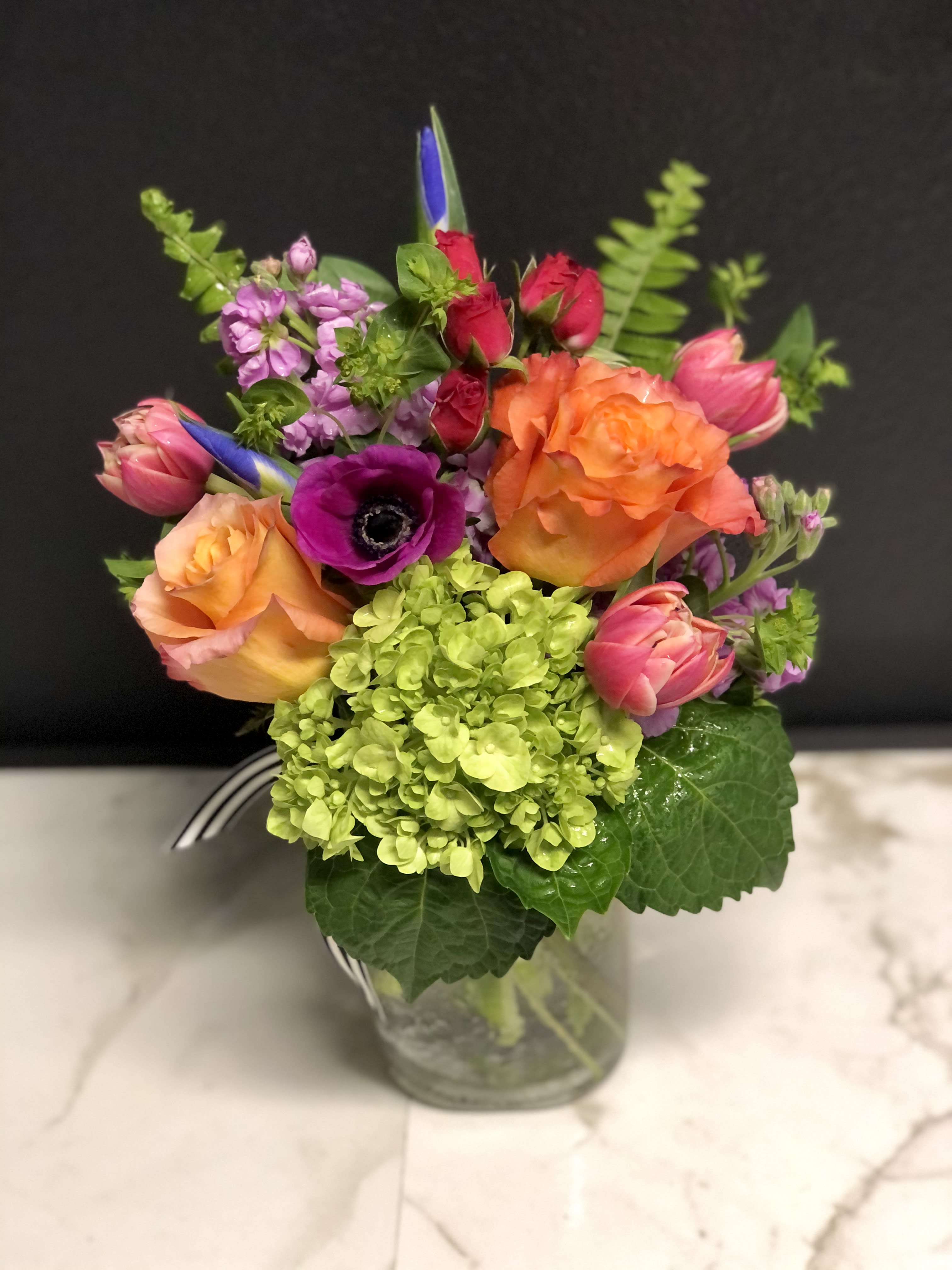 Vibrant Bloom Jar  - A bright, colorful, garden mix with season's prettiest blossoms. Arranged in our clear glass Bloom jar.              Overall design is approximately 12" tall.   Floral varieties may vary but will be of similar quality and style.  