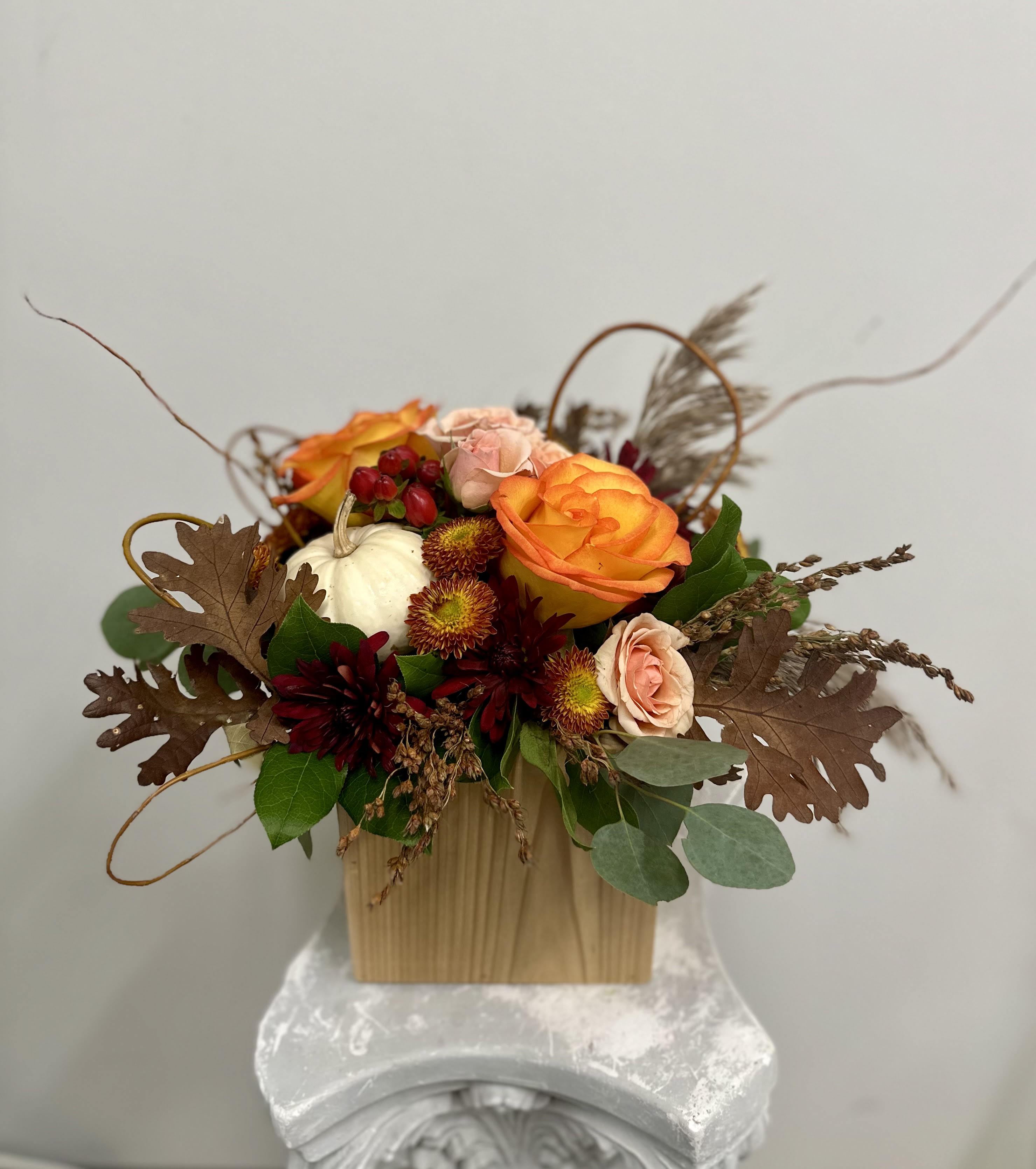 Give a Thanks by Westford Florist Art by Veny - Elevate your holiday gatherings with Give a Thanks by Westford Florist Art by Veny. This exquisite arrangement is beautifully crafted in a natural white cedar keepsake box, designed to enhance your festive table setting. Featuring an enchanting blend of peach and orange roses, delicate spray roses, striking protea, and rich red hypericum berries, this centerpiece embodies the essence of autumn. Complemented by vibrant fall-colored poms and thoughtfully arranged dry accents—including a charming real mini pumpkin—this piece brings warmth and gratitude into any home. The lush greenery adds depth, creating an inviting atmosphere that speaks to the heart of the season. Perfect for expressing appreciation or adding beauty to your celebration, this stunning floral art piece is a true testament to thoughtful design.