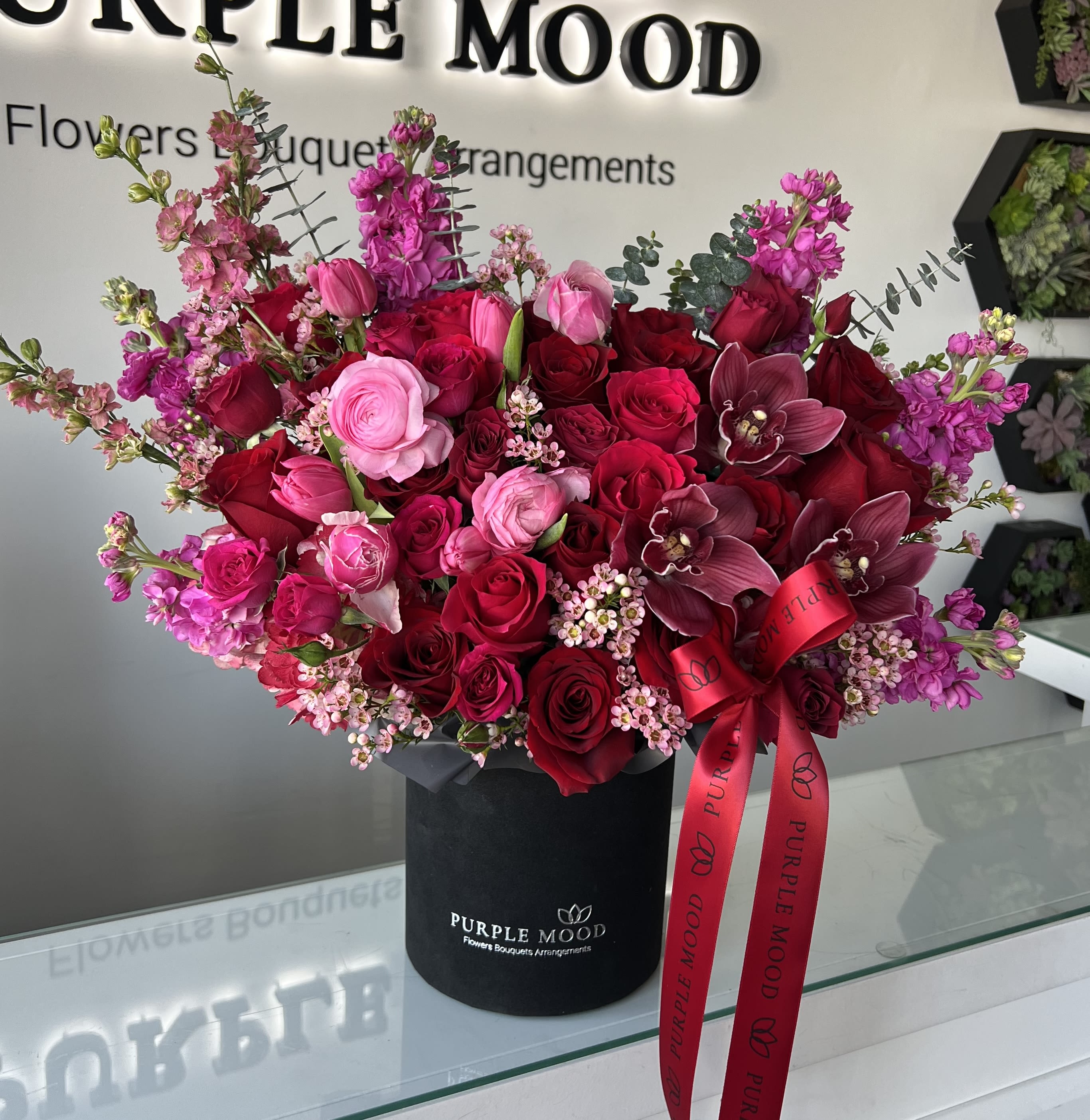 Fire mix box - Standard - Container size D6.75'x H7.5'  Deluxe - Container size D8.25'x H9.5'  Premium - Container size D10.5'x H12.25'  Ignite the passion with our Fire Mix Box – a luxurious arrangement that blends vibrant shades of red and pink to create a stunning display of elegance and romance. Featuring premium red roses, delicate pink ranunculus, exotic orchids, and charming accent flowers, this bouquet is presented in a sleek black box adorned with a signature Purple Mood ribbon. Perfect for Valentine’s Day, anniversaries, or any heartfelt celebration, the Fire Mix Box is designed to leave a lasting impression.  Let the beauty of this arrangement speak for your love and appreciation.
