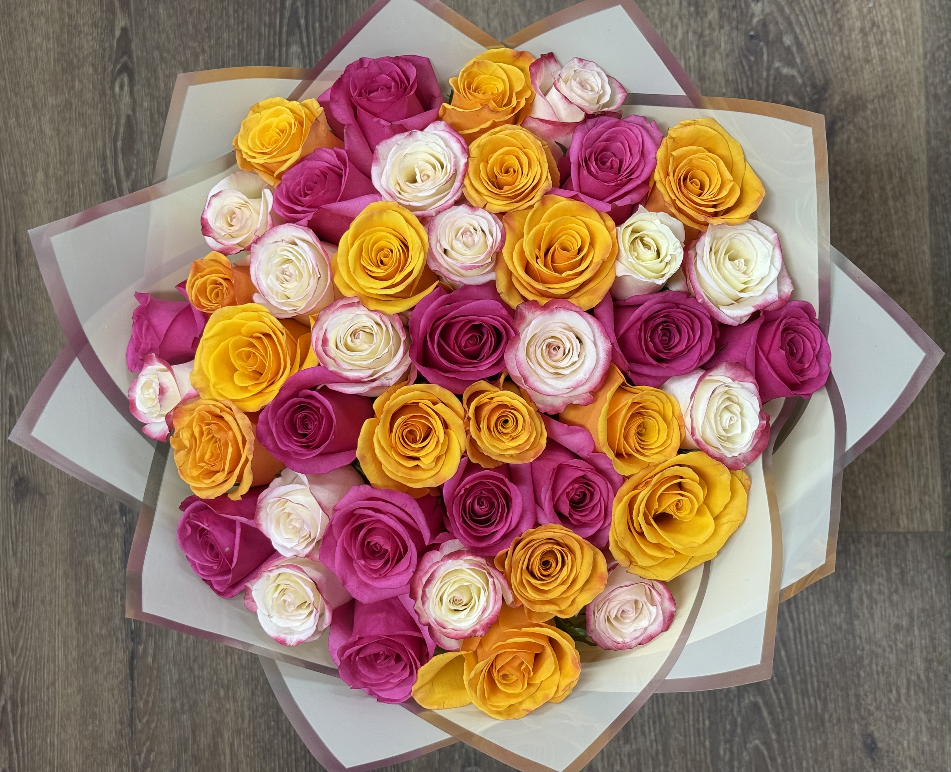 Golden Petal Party Bouquet - The Golden Petal Party is a bouquet that features a bright mix of yellow, hot pink, and white roses. This arrangement uses a cheerful spring color palette and is finished in a layered yellow Korean paper wrap with silver borders.