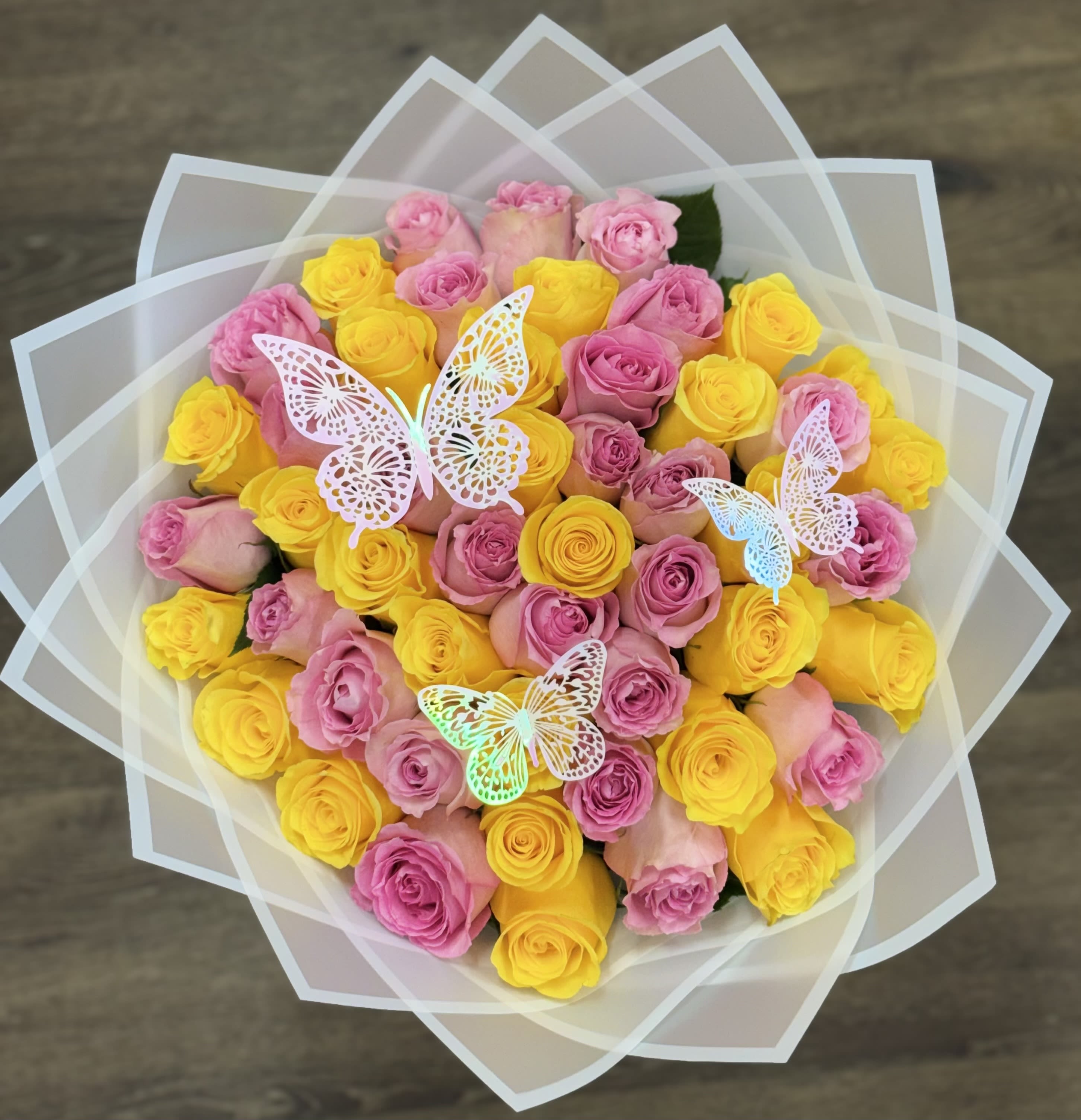 Mariposa Garden Bouquet - The Mariposa Garden features a dense mix of pink and yellow roses. This arrangement includes three multi-colored iridescent butterfly accents and is finished in a layered white Korean paper wrap with a white border. (Butterflies Included)