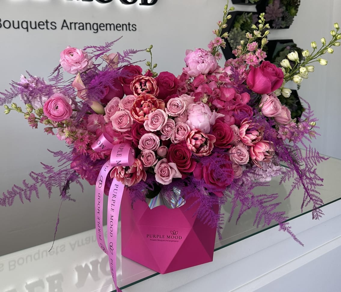 Milkshake Geometric Box - Container size - D7.75’x H8.25′  All around arrangement with no lid in back. Box includes wet floral foam inside, box doesn’t require vase.  Vibrant and full of energy, the Milkshake Geometric Box is a striking mix of hot pinks, blush, and deep magentas. Styled in a modern geometric box, it’s both playful and luxurious — a perfect gift for someone who loves bold colors and unforgettable surprises.  Key Features:     •    Presented in a chic geometric box for a modern look     •    Finished with a signature ribbon for extra elegance     •    Designed with rich pink tones for a vibrant effect     •    A statement gift for birthdays, celebrations, or romantic gestures