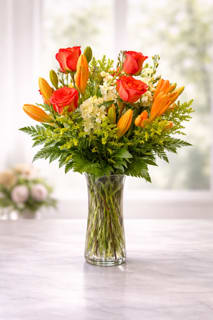 Chino's Peach Glow - What’s pretty in peach? This rich mix of orange lilies, peach roses and lovely blossoms, simply arranged in a clear glass vase, will create a warm glow in any setting. A charming bouquet for anyone who loves flowers.