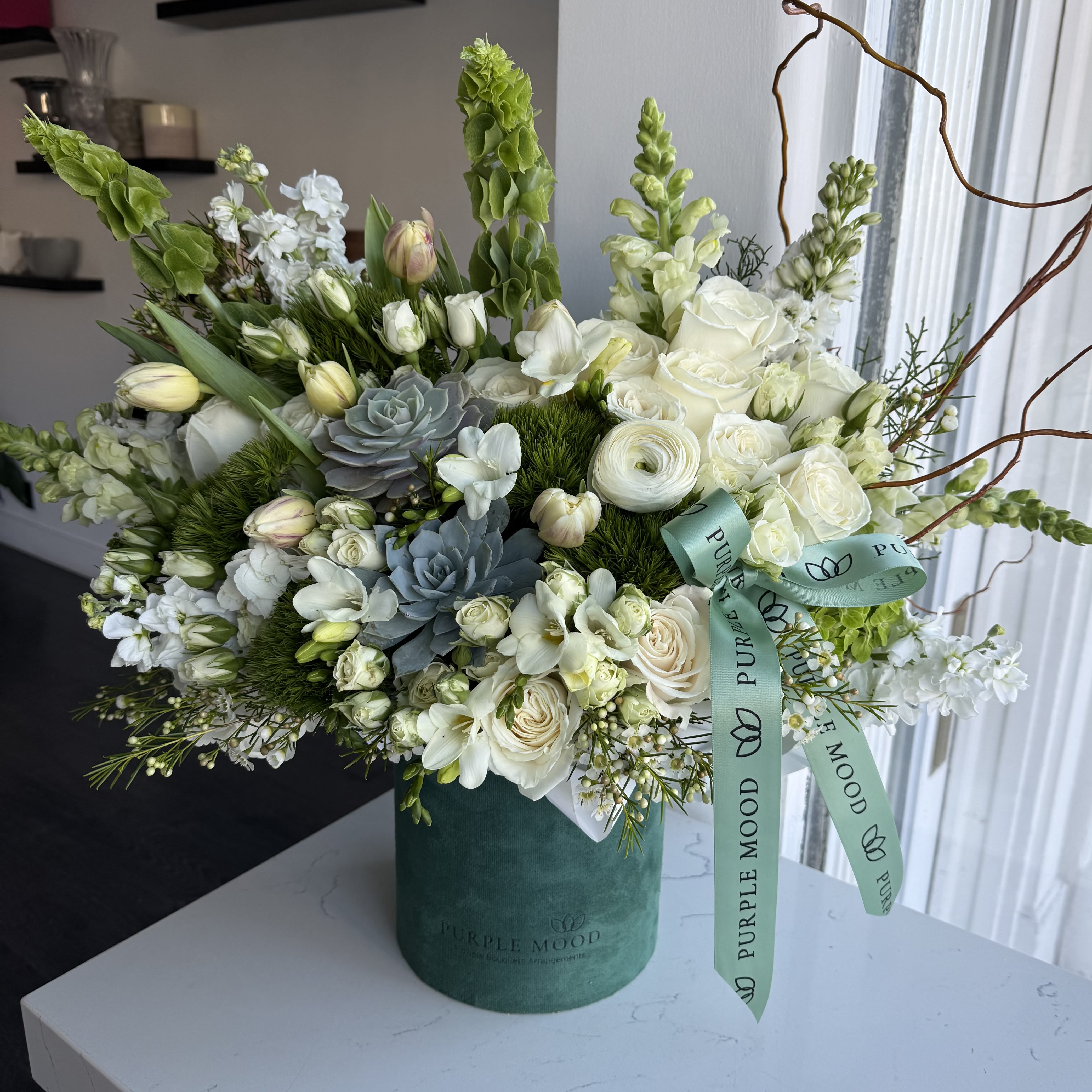 Nature Green Box - Container size - D6.75'x H7.5'  Bring the outdoors in with the Nature Green Box, a lush blend of soft whites, vibrant greens, and textured accents. Designed in a deep green velvet hat box, this arrangement has a fresh, earthy feel — perfect for nature lovers or as a modern décor statement.  Key Features:     •    Presented in a deep green velvet hat box     •    Finished with an elegant ribbon for a refined look     •    A refreshing mix of textures and natural tones     •    Great for home styling, birthdays, or thoughtful gifts