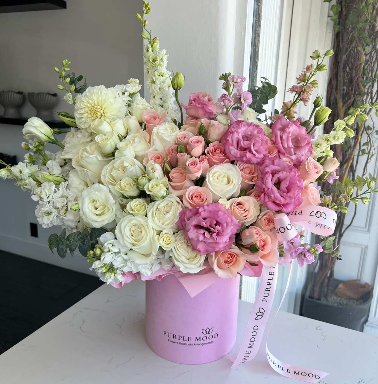 Pink Box - Standard container size D6.75'x H7.5' Deluxe container size - D8.25'x H9.5' Premium container size - D10.5'x H12.25'  Delicate and graceful, the Pink Box is a soft celebration of love and charm. With its blend of blush pinks, creamy whites, and gentle blooms, this arrangement feels like a sweet embrace. Presented in a pastel pink hat box, it’s an elegant choice for any occasion.      •    Romantic mix of pink and ivory tones     •    Presented in a chic pastel pink hat box     •    Designed for birthdays, anniversaries, or thoughtful surprises     •    A timeless gesture of elegance and affection  Front side arrangement with lid in the back. Box includes wet floral foam inside, box doesn't require vase.