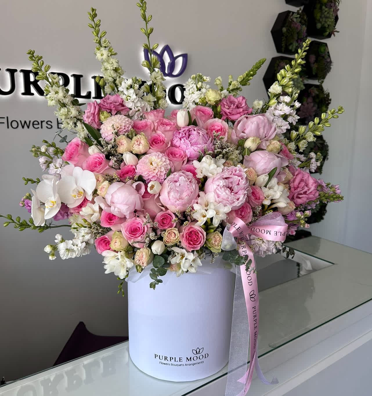 Pretty Box - Container size - D10.5'x H12.25'  Pretty Box Luxurious and overflowing with beauty, the Pretty Box is designed to leave a lasting impression. Featuring a lavish mix of pink peonies, roses, orchids, and seasonal blooms, this arrangement bursts with romance and elegance. Presented in a chic signature hatbox, it’s a statement of pure sophistication.      •    Designed in an elegant signature Purple Mood hatbox     •    Generously sized for maximum impact     •    Perfect for grand celebrations, anniversaries, or gifting unforgettable moments