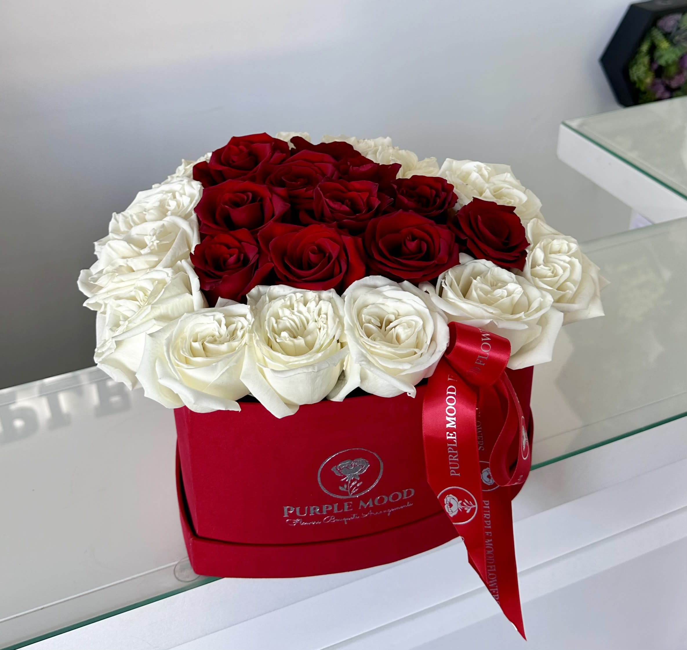 Red Heart Box - Approximately 28-33 stem. Box size: ~ 11” x 11”  Red Heart Classic and romantic, the Red Heart is designed to symbolize pure love and devotion. With its bold red center framed by soft white blooms, this elegant heart-shaped box makes a timeless statement of affection.      •    Presented in a signature Purple Mood box with ribbon detail     •    Compact, chic, and impactful design     •    Perfect for anniversaries, Valentine’s Day, or romantic surprises