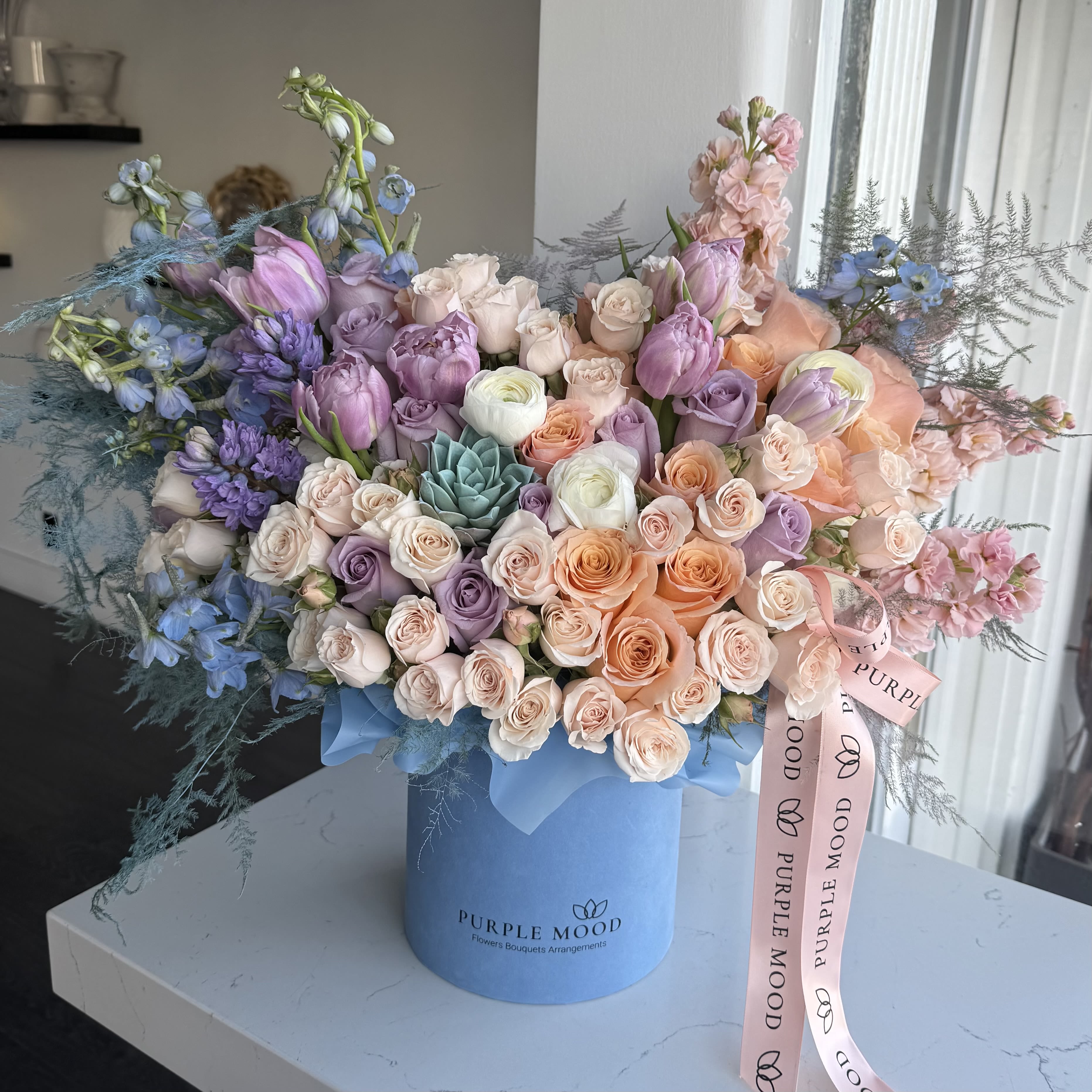 Shimmer Box - Standard container size - D6.75'x H7.5'  Deluxe container size - D8.25'x H9.5'  Premium container size - D10.5'x H12.25'  Shimmer Box A dazzling burst of pastel elegance, the Shimmer Box is a radiant arrangement that feels soft, dreamy, and enchanting. With its blend of delicate hues, it brings a touch of magic and sophistication to any occasion.      •    Arranged in a chic velvet hatbox for a polished look     •    A pastel color palette that feels fresh and luminous     •    Available in Standard, Deluxe, and Premium sizes     •    Perfect for birthdays, celebrations, or simply brightening someone’s day