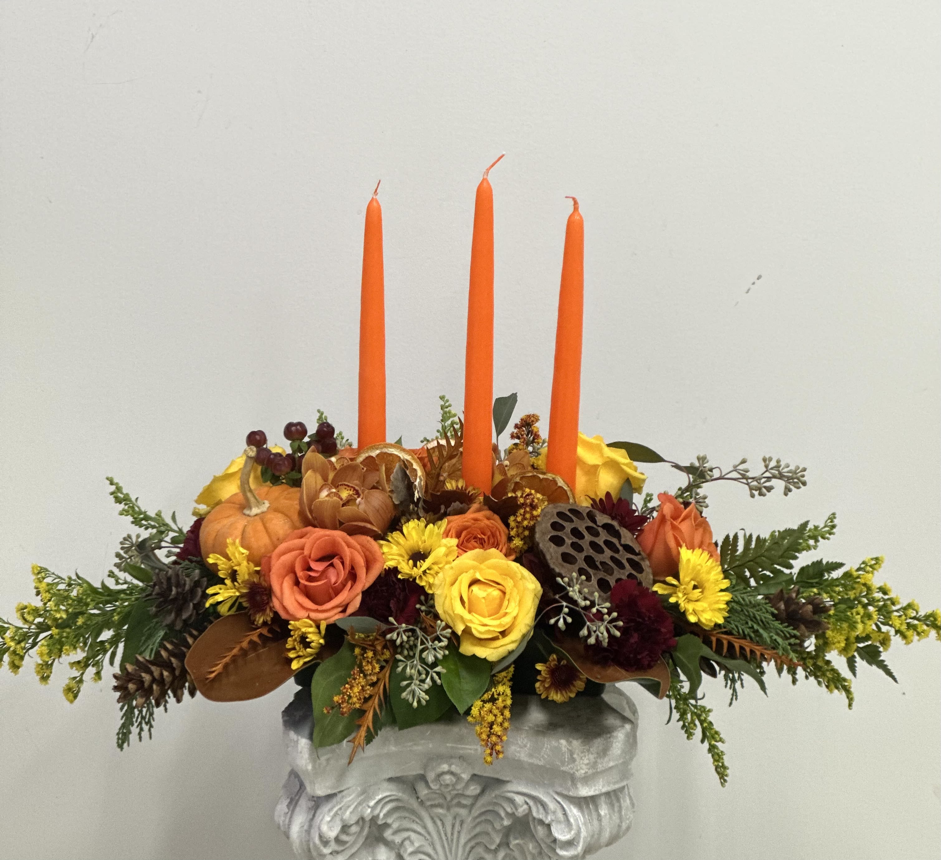 Harvest Glow Premium Centerpiece by Westford Florist Art by Veny - Elevate your autumn gatherings with the Harvest Glow Premium Centerpiece by Westford Florist Art by Veny. This exquisite arrangement captures the essence of fall, featuring a vibrant blend of orange and yellow roses elegantly paired with charming mini pumpkins and lush hypericum berries. Rich foliage completes the look, bringing a touch of nature indoors. Tall candles flicker invitingly, creating a warm ambiance that enhances any setting. For those seeking a touch of sophistication, our premium option showcases delicate orchids that elevate this centerpiece to an unparalleled level of elegance—perfect for making lasting impressions at dinner parties or festive celebrations. Transform your space into a seasonal sanctuary with this stunning display from Westford Florist.