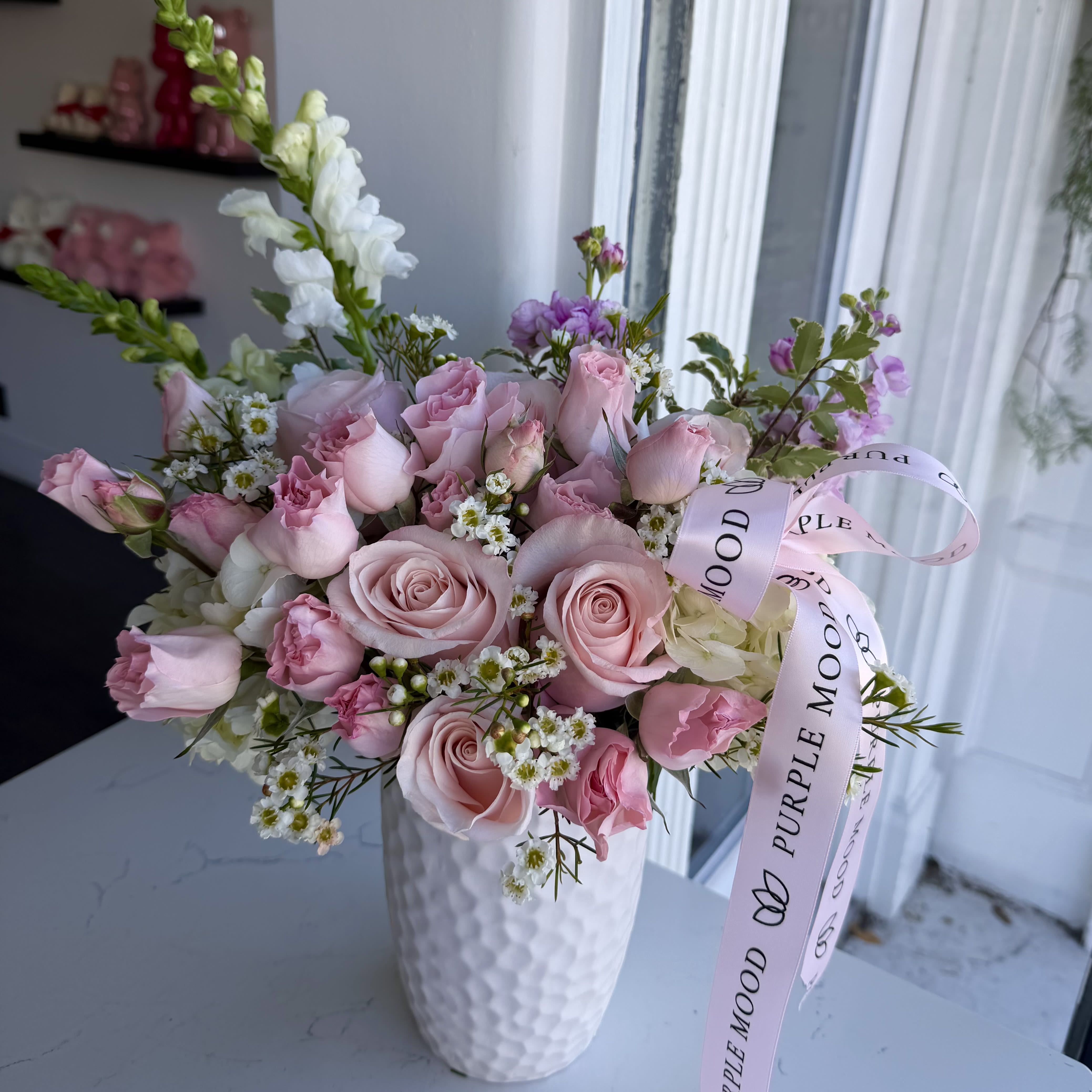 Enchanted Garden Vase - A soft pastel dream captured in a vase — romantic, airy, and full of charm. Shades of blush, lavender, and cream come together in a perfectly balanced design that feels both elegant and effortless. Finished with a satin ribbon, this arrangement brings a sense of calm beauty to any space or occasion.      •    Handcrafted in gentle pastel tones     •    Presented in a modern white vase     •    Finished with a soft satin ribbon     •    Perfect for birthdays, celebrations, or thoughtful gestures