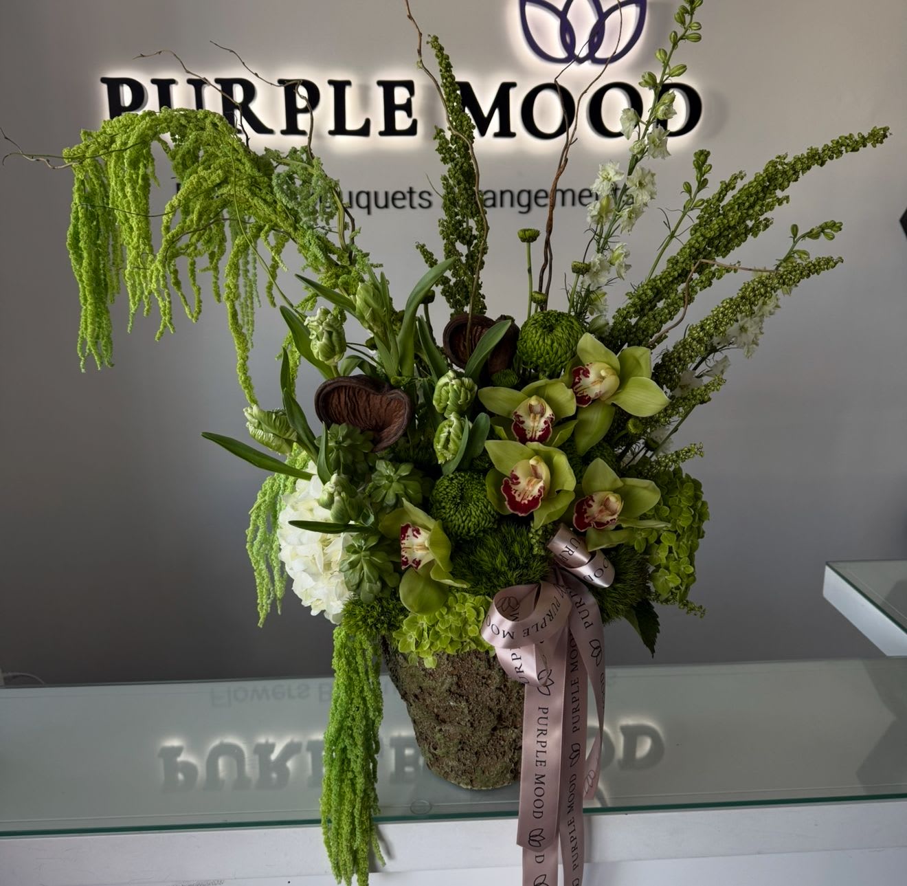 Forest Vase - Bring the magic of nature indoors with our Forest Vase, a lush and enchanting arrangement that captures the essence of a woodland retreat. Filled with vibrant green blooms, exotic orchids, and earthy textures, this piece is designed to impress with its bold and natural elegance. Perfect for sophisticated gifts, corporate settings, or adding a striking statement to any space.      •    Exotic Green Cymbidium Orchids for a luxurious touch     •    Hydrangeas &amp; Greenery to add lush volume and depth     •    Chrysanthemums &amp; Seasonal Blooms for balance and texture     •    Arranged in a natural moss-textured vase for a forest-inspired look     •    Ideal for luxury gifts, office décor, or statement centerpieces