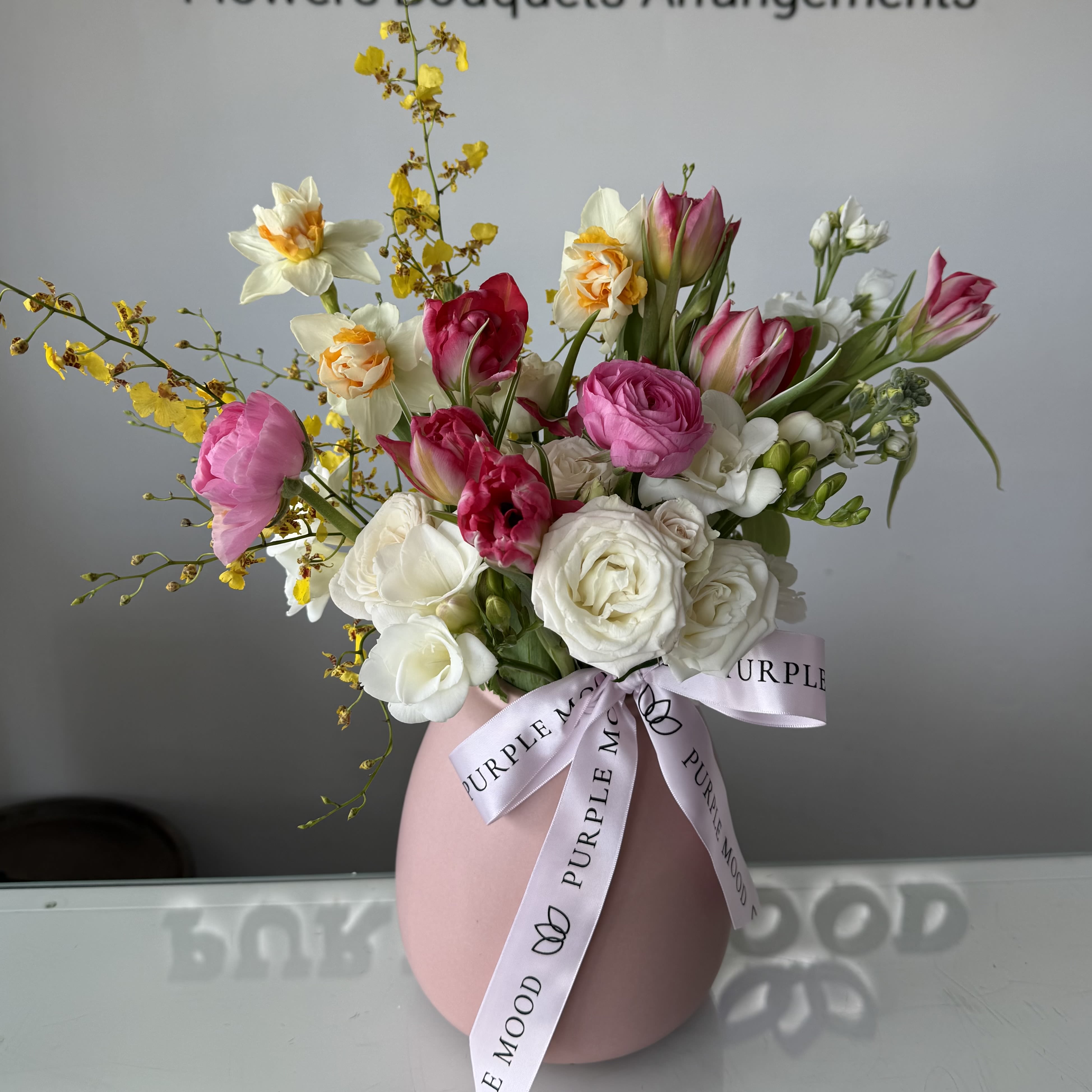 Pink Blossom Vase - Soft, romantic, and full of spring charm — our Pink Blossom Vase is a celebration of delicate color and seasonal beauty.  This arrangement features a graceful blend of pink tulips, ranunculus, creamy roses, fresh freesia, cheerful daffodils, and light seasonal accents, thoughtfully designed in a modern blush vase.  Airy textures and gentle movement create a fresh garden-inspired look, perfect for birthdays, spring celebrations, or simply brightening someone’s day.  Vase is included.  Flowers may vary slightly based on seasonal availability while maintaining the overall style and color palette.