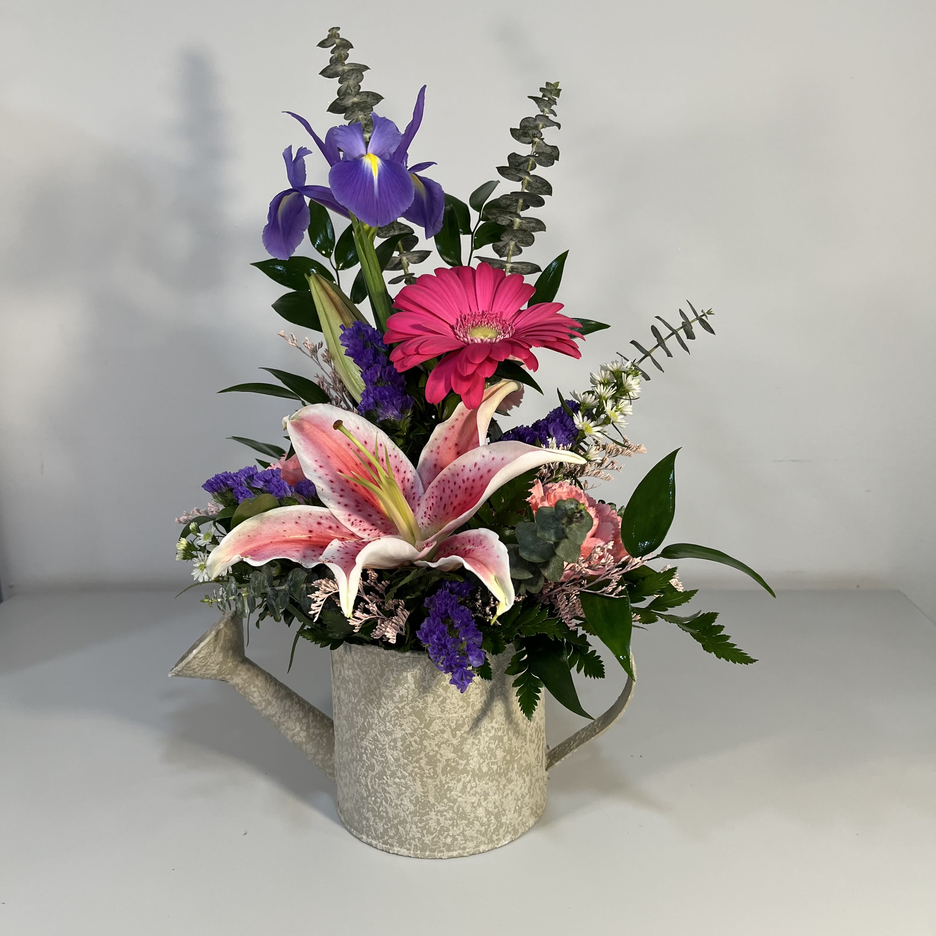 Spring Sprinkle - Watering can filled with Iris, Gerbera Daisy, Oriental Lily,  Carnation and filler. (Colors of Flowers and Watering Can vary by availability)