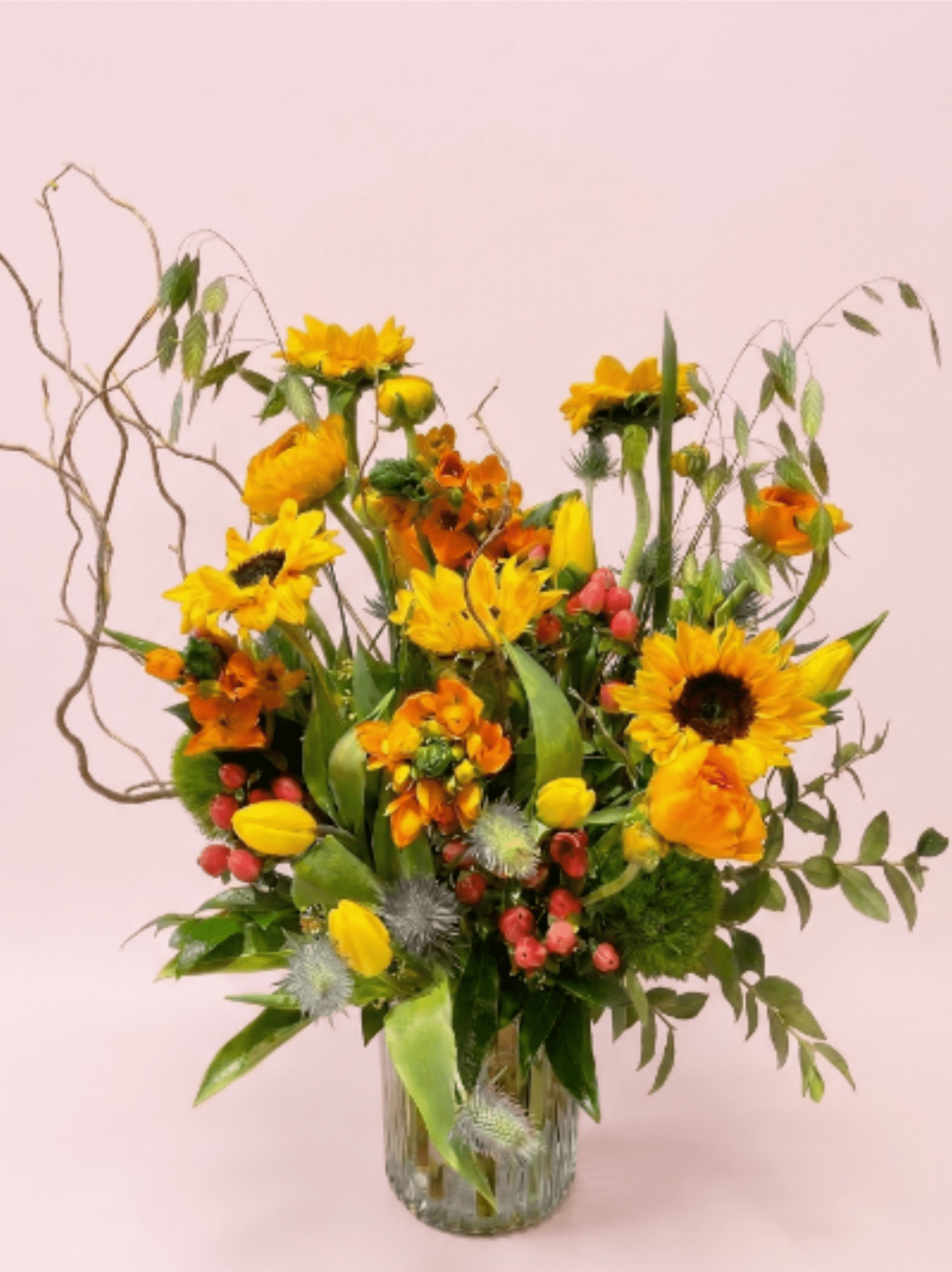 Tall yellow and orange flower arrangement with sunflowers in a clear glass vase.