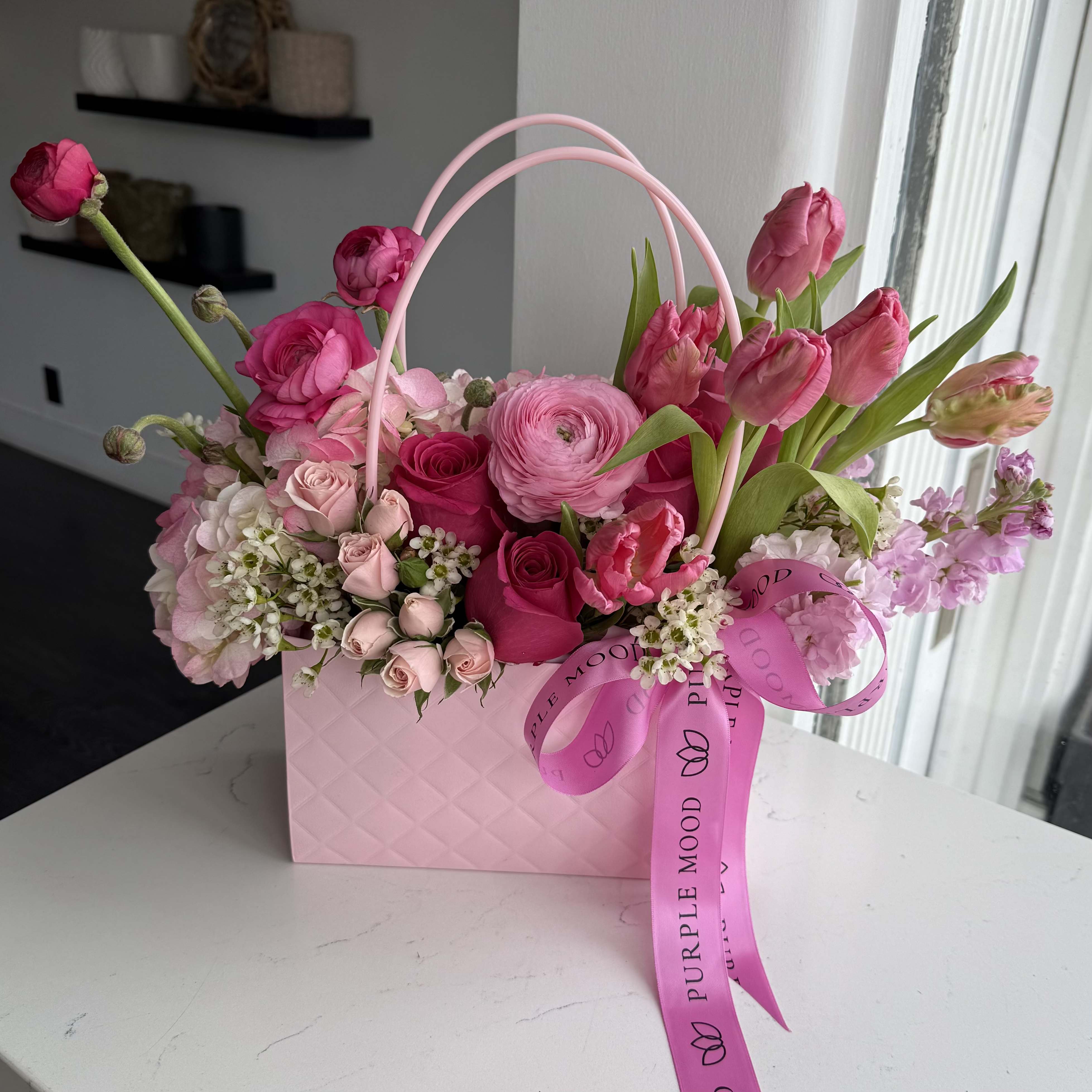 Mini Bag Pink - (Flowers can be different)  Chic and charming, the Mini Bag Pink is a delightful arrangement of romantic pink and red tones, styled in a quilted pink bag with handle. Compact yet full of beauty, it’s the perfect gift to brighten someone’s day or add a touch of love to any occasion.  Key Features:     •    Finished with a signature ribbon for a playful detail     •    Compact and trendy size, perfect for desks, coffee tables, or bedside tables     •    A sweet and thoughtful gift for birthdays, thank-yous, or just because