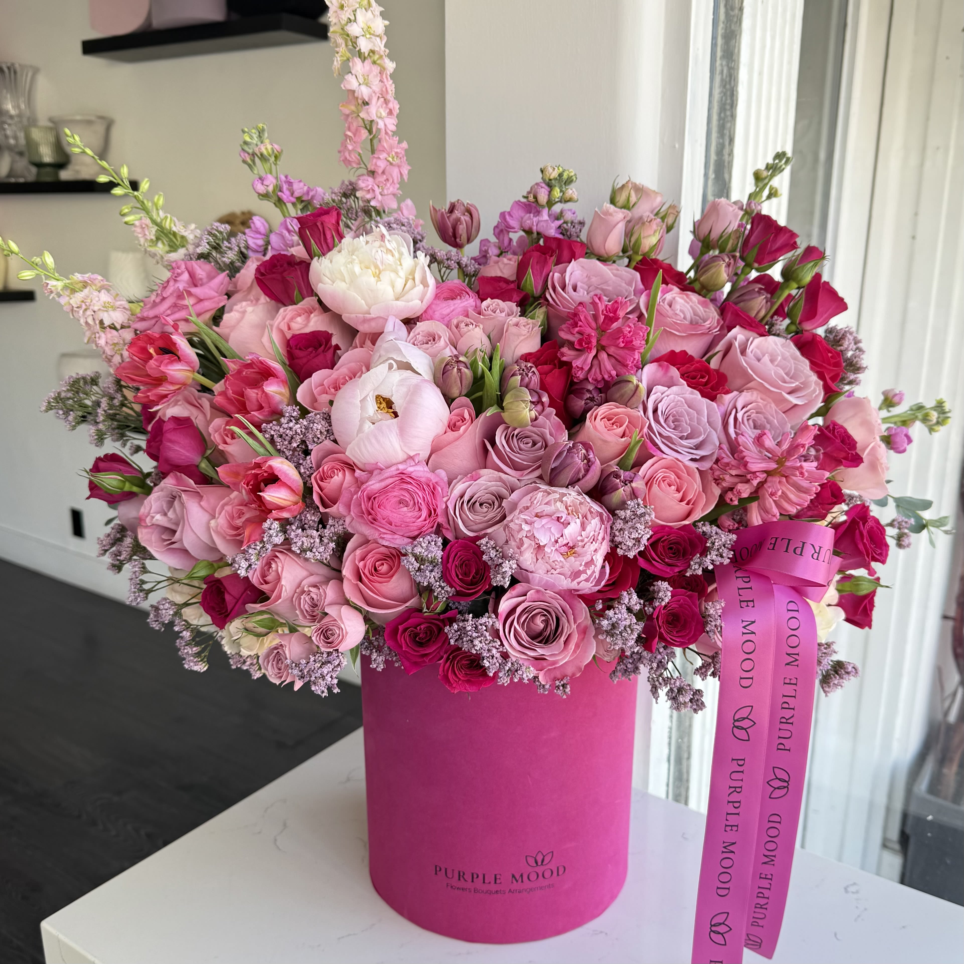 Paradise cloud - Container size - D8.25'x H9.5'  The Paradise Cloud is pure floral bliss — a lavish burst of pink shades that feels both romantic and dreamy. Styled in a bold fuchsia box, this arrangement is designed to impress and bring joy at first sight.  Key Features:     •    Luxurious full arrangement in a vibrant pink box     •    A romantic mix of soft and bold pink tones     •    Finished with a signature ribbon for elegance     •    Perfect for anniversaries, birthdays, or unforgettable surprises