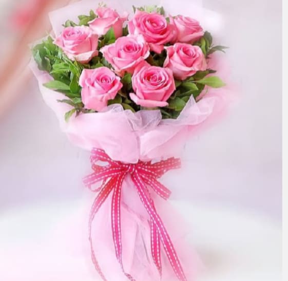 Sweet Pink Roses - A lush dome of medium pink roses arranged in a tight, hand-tied bouquet gives this flower arrangement an immediate, heartwarming impression - perfect as a birthday bouquet, anniversary roses, romantic gesture, or a thoughtful way to say "I'm thinking of you." The cluster of open pink blooms reads as sweet and feminine; paired with pale green foliage, it creates a gentle contrast that makes the pink tones feel even softer and more affectionate for the person you're celebrating.  Wrapped in layers of soft, sheer pink paper, pale pink tissue and romantic pink tulle, the bouquet has a cloud-like, airy presentation that's both playful and elegant. A bright pink ribbon with white stitching (plus coordinating pink ribbon and tissue wrap) is tied in a neat bow at the base, finishing the look with a youthful, handcrafted touch. Sized as a full, rounded hand-tied bouquet, it's an easy-to-give gift that will make the recipient feel genuinely seen and cherished - order for same-week delivery to brighten someone's day.