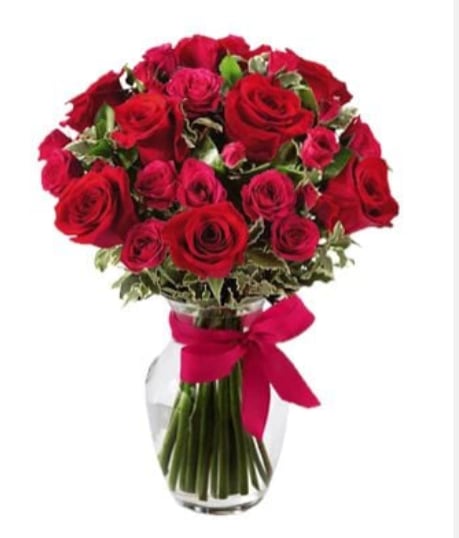 Passionate Heart Bouquet - A lush, domed cluster of rich red roses and delicate spray roses, this flower arrangement is built for romantic moments - an ideal anniversary roses bouquet or Valentine's Day gift that reads as classic, intimate, and heartfelt. The dense, velvety red blooms create an immediate visual impact so the person you're thinking of will feel adored the moment they see it.  Tightly packed standard roses and spray roses form a rounded, full shape with variegated green foliage peeking between the heads for contrast and texture. Stems show cleanly through a simple clear glass vase, and the neck is finished with a vibrant red bow and a playful pink satin ribbon for an extra touch of romance. The arrangement's compact, domed silhouette makes it easy to display on a table or desk while keeping a polished, timeless look.  Perfect for saying "I love you," celebrating an anniversary, or marking a special milestone, this bouquet delivers warmth and devotion without fuss. Order with same-day delivery where available; to keep blooms looking their best, refresh the water every 2-3 days and trim stems slightly when re-cutting into fresh water.
