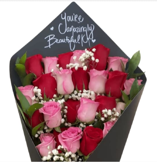 Rose Bouquet - Dense rows of red and pink roses rise upright from a matte black, envelope-style gift box, creating a modern, dramatic statement perfect for a romantic bouquet or anniversary roses. The tall back panel bears a handwritten-style white message that reads like a personal note, so the person you're thinking of will feel genuinely seen the moment they open it. This design reads intentional and intimate-ideal for Valentine's Day, milestone celebrations, or any moment you want to mark with romance.  Tightly packed roses alternate in rich red and soft pink tones, with clusters of small white filler flowers tucked between blooms to add delicate texture and crisp contrast against the dark box. The black gift box itself doubles as presentation and keepsake, its matte finish making the colors pop while the printed message panel gives the arrangement a finished, personal touch. Sized to sit on a table or bedside, the upright arrangement offers strong visual height without sprawling stems; care is simple-keep in a cool spot away from direct sun and refresh water as needed if stems are placed in water inside the box.  This is the kind of bouquet that reads as thoughtful and romantic for a partner, spouse, or someone you're wooing-an unmistakable expression of affection that arrives ready to impress. Add a treasured note on the printed panel when ordering to make the sentiment unmistakably yours.