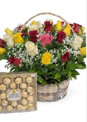 Golden Love Rose Basket - A radiant mix of red, yellow, cream and pink roses arranged in a rustic woven basket makes this flower arrangement a joyful choice for an anniversary bouquet or romantic gift. The Golden Love Rose Basket is designed to make the person you're thinking of feel cherished-bright yellow blooms for warmth, deep red for devotion, and soft pink and cream for tenderness-paired with a box of gold-wrapped chocolates for an extra celebratory touch.  The arrangement features roses rising above a dense, rounded base and accented with small clusters of delicate white filler flowers that add light texture and contrast. Displayed in a handled woven basket, the presentation feels both classic and homey; the included clear-front box of individually wrapped chocolates sits beside the basket for an elegant finishing touch.  Perfect for anniversaries, Valentine's Day, or to say "I love you" in a memorable way, this set arrives ready to gift and creates a bright, fragrant centerpiece wherever it's placed. Order with standard sizing in mind-the basket's handle frames the arrangement for easy carrying-and enjoy simple care: keep water fresh and trim stems if you transfer flowers to vase to extend their bloom.