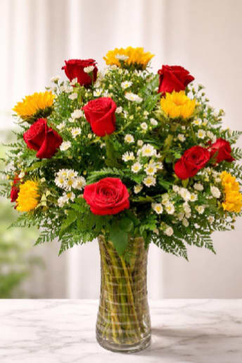 Sunset Garden Vase - Bold red roses and sunny yellow sunflowers create an immediate, heartwarming impression in this flower arrangement-perfect as a birthday bouquet or anniversary gift that feels both joyful and romantic. Bright white daisies peek through the larger blooms, softening the contrast and giving the person you're thinking of a cheerful, uplifting surprise that reads as celebration or sincere affection.  Arranged in a rounded, upright silhouette, the blooms sit in a clear glass vase that showcases the clustered green stems for a fresh, garden-picked look. The palette of red, yellow, green, and white brings high-contrast visual energy balanced by delicate daisy texture; the vase size and stem length work together to make a table-ready centerpiece that still feels intimate.  Choose this for birthdays, congratulations, or an everyday "thinking of you" moment when you want someone to feel seen and celebrated. The arrangement arrives ready to display-trim stems and refresh water every couple of days to keep the roses, sunflowers, and daisies looking their best.