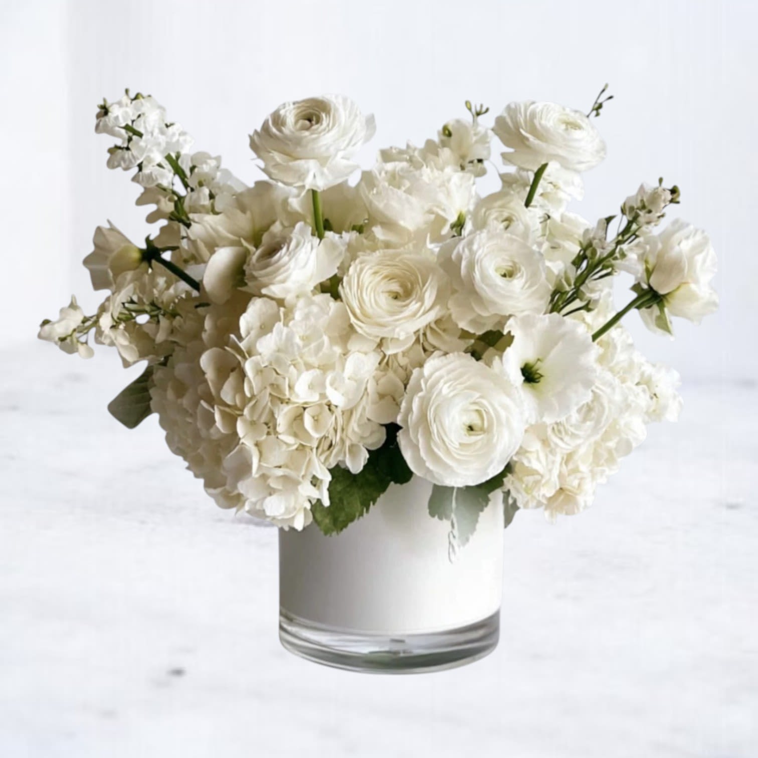 Monochrome Garden - Monochrome Garden is a layered all-white composition featuring ranunculus, hydrangea, lisianthus, and fragrant stock arranged in a modern white vessel. Subtle variations in bloom shape and texture create depth while the monochromatic palette keeps the design fresh and architectural.  Refined without feeling formal, this arrangement is ideal for moments that call for quiet elegance — whether you’re offering support, marking a new chapter, or sending something beautifully understated.  Available for same-day flower delivery in Houston and surrounding areas.