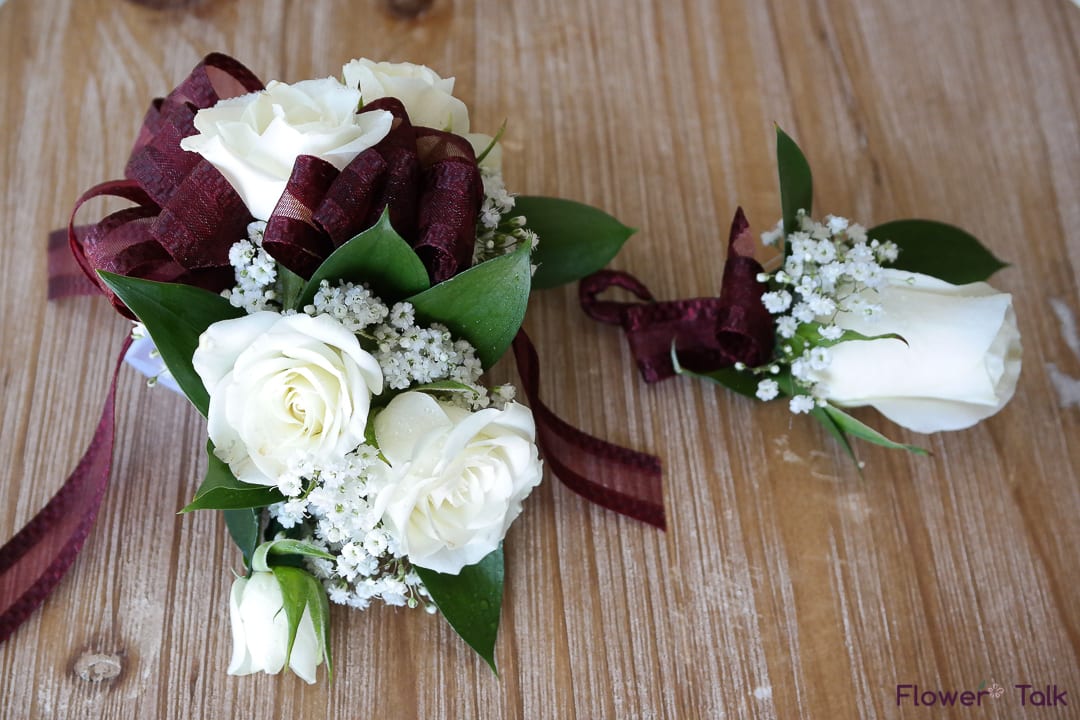 Prom Wrist Corsage &amp; Boutonniere Set - Maroon Ribbon &amp; White Flowers - Impress your date with this classy corsage.  Consisting of a maroon colored ribbon &amp; white spray roses.  The wrist strap will be a white velcro strap adjustable to the size of the wrist.