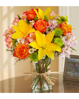 Mixed bouquet of yellow lilies, orange roses and pink flowers in a glass vase with a raffia bow