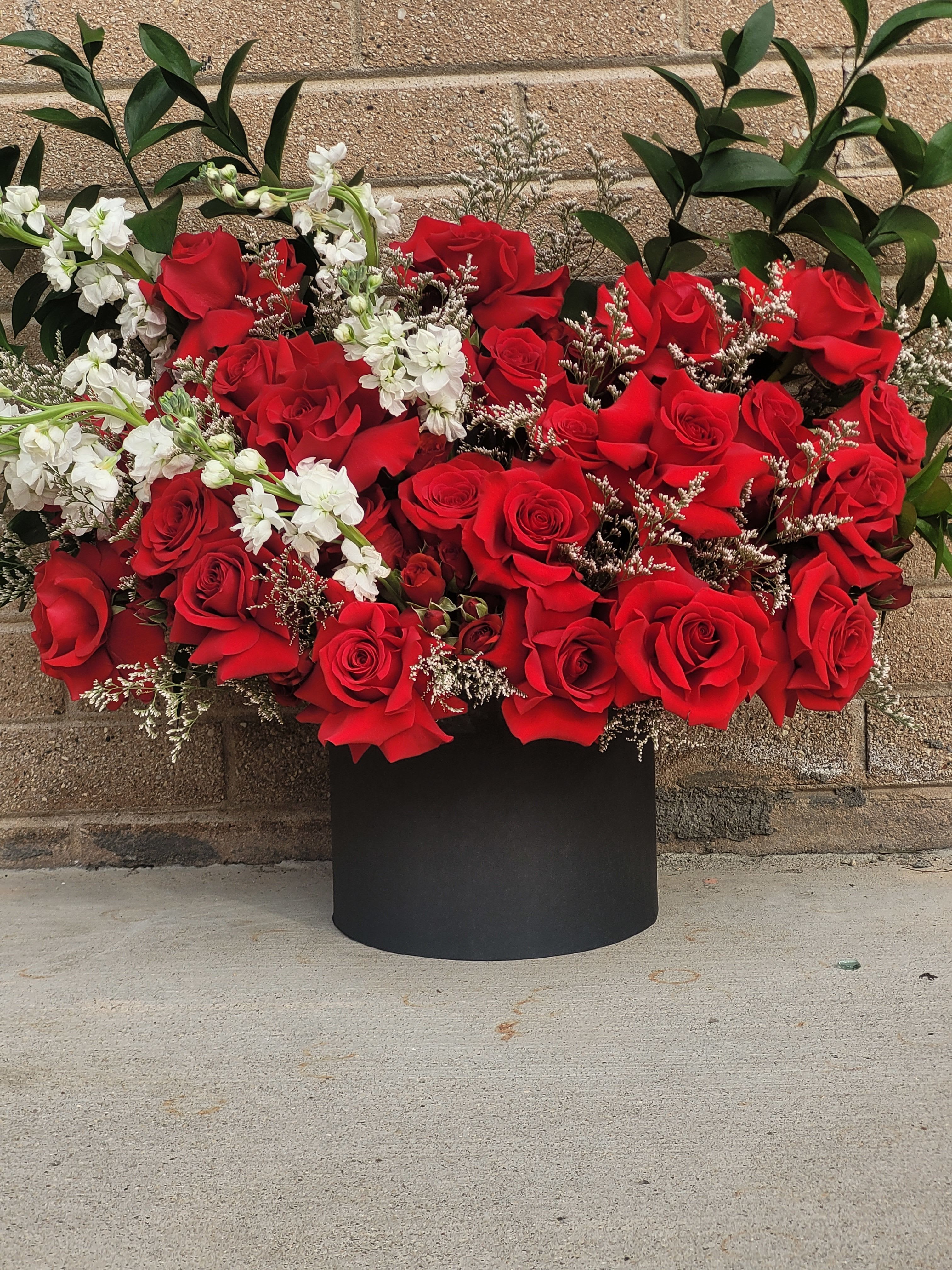 Love in Bloom - A bold and romantic arrangement of rich red roses accented with delicate white blooms and lush greenery, designed in a sleek black box for a modern, luxurious statement. 