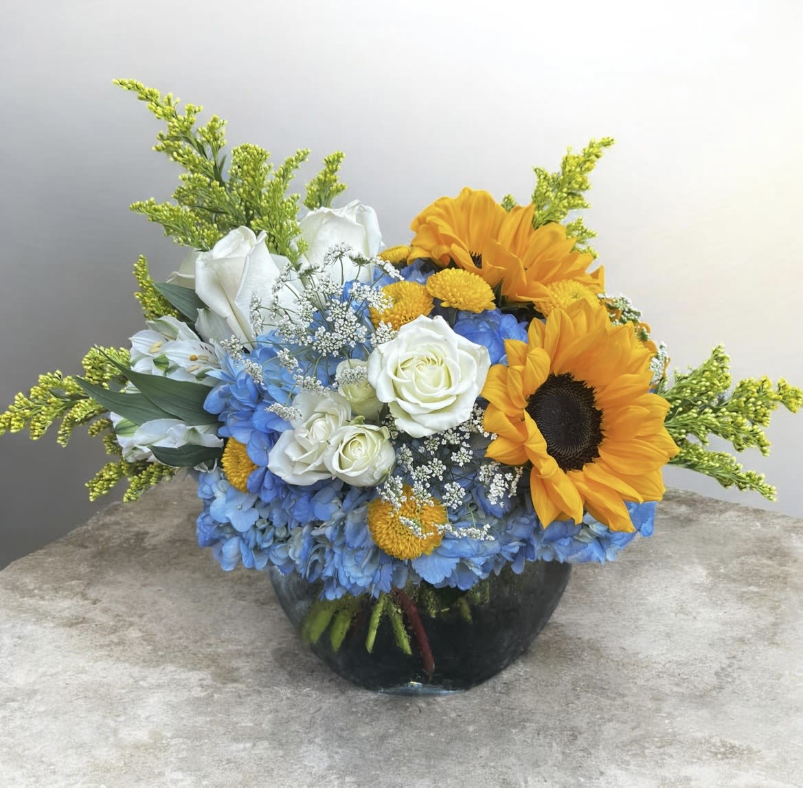 Blue Beauty  - This beautiful arrangement is in an 8 in bubble bowl it has hydrangea's, roses, sunflowers, alstroemeria, spray roses, Queens Ann’s lace, daises and mums, with little touches of wax flower and solidago. 