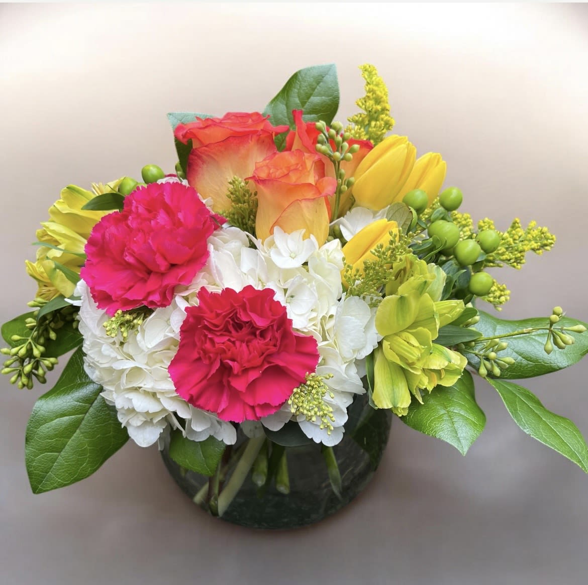 Paradise  - This arrangement has hydrangea, orange roses, yellow tulips, yellow alstroemeria, hot pink carnations, green Hypericum, Solidago, and beautiful greenery