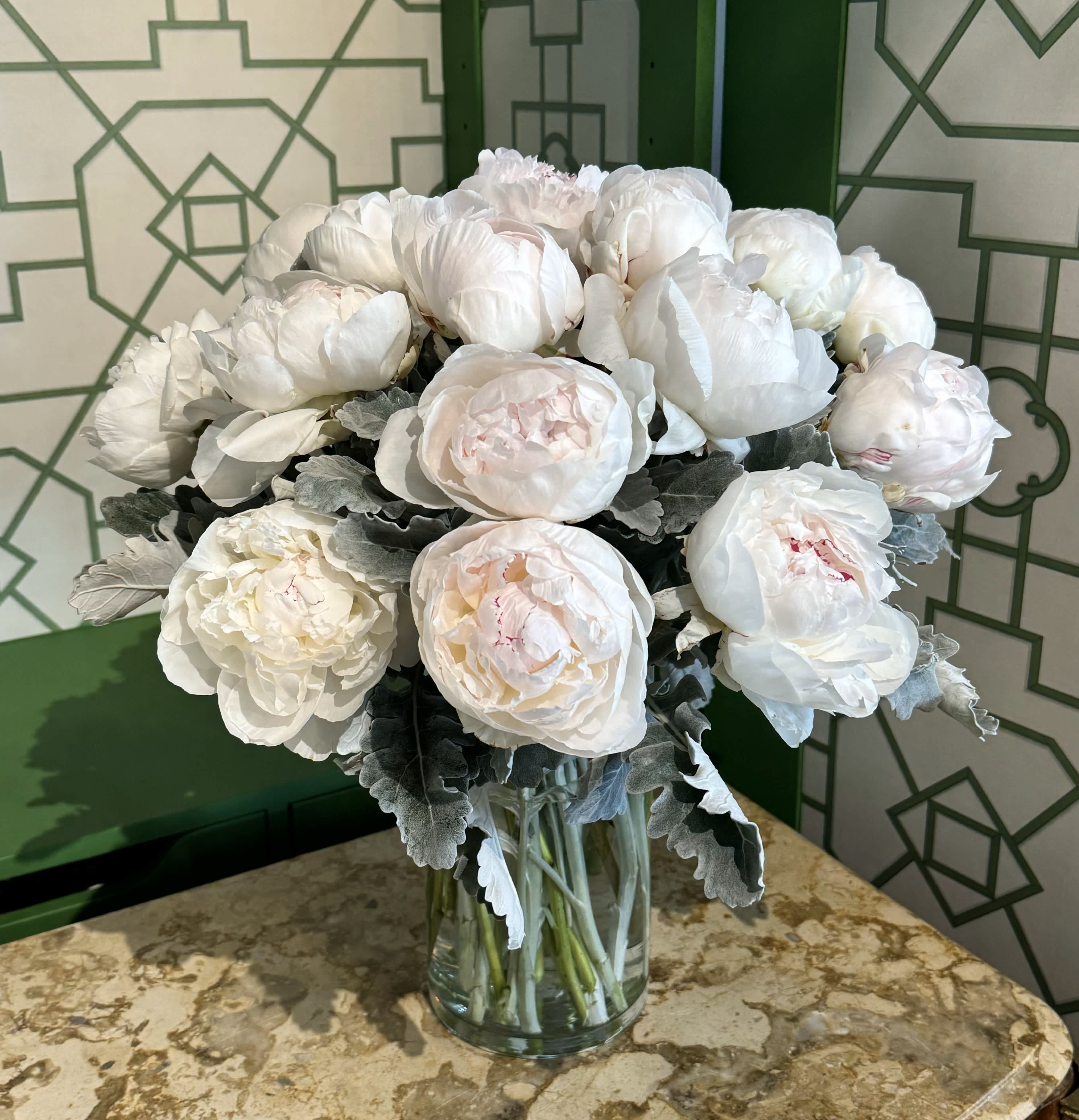 Peony Paradise - Indulge in the beauty of Peony Paradise, where 20 luxurious white peonies take center stage, surrounded by soft accents of dusty miller. Arranged in a sleek 10-inch-tall cylinder vase, this elegant composition brings timeless charm and sophistication to any space. Whether you’re treating yourself or gifting it to someone special, Peony Paradise captures the pure, graceful essence of these stunning blooms.  Please note: Peony color may vary based on seasonal availability, ensuring each arrangement is unique.   Freshness Guarantee: At Belden's Florist, we stand behind the quality of every arrangement. Our flowers are guaranteed to remain fresh and beautiful for 3–5 days after delivery. While cut flowers may naturally begin to wilt beyond this timeframe, we ensure that only the freshest blooms are selected and expertly arranged to bring joy and elegance to your space. To extend their life, we recommend refreshing the water in your vase daily, allowing your flowers to stay hydrated and continue to dazzle.