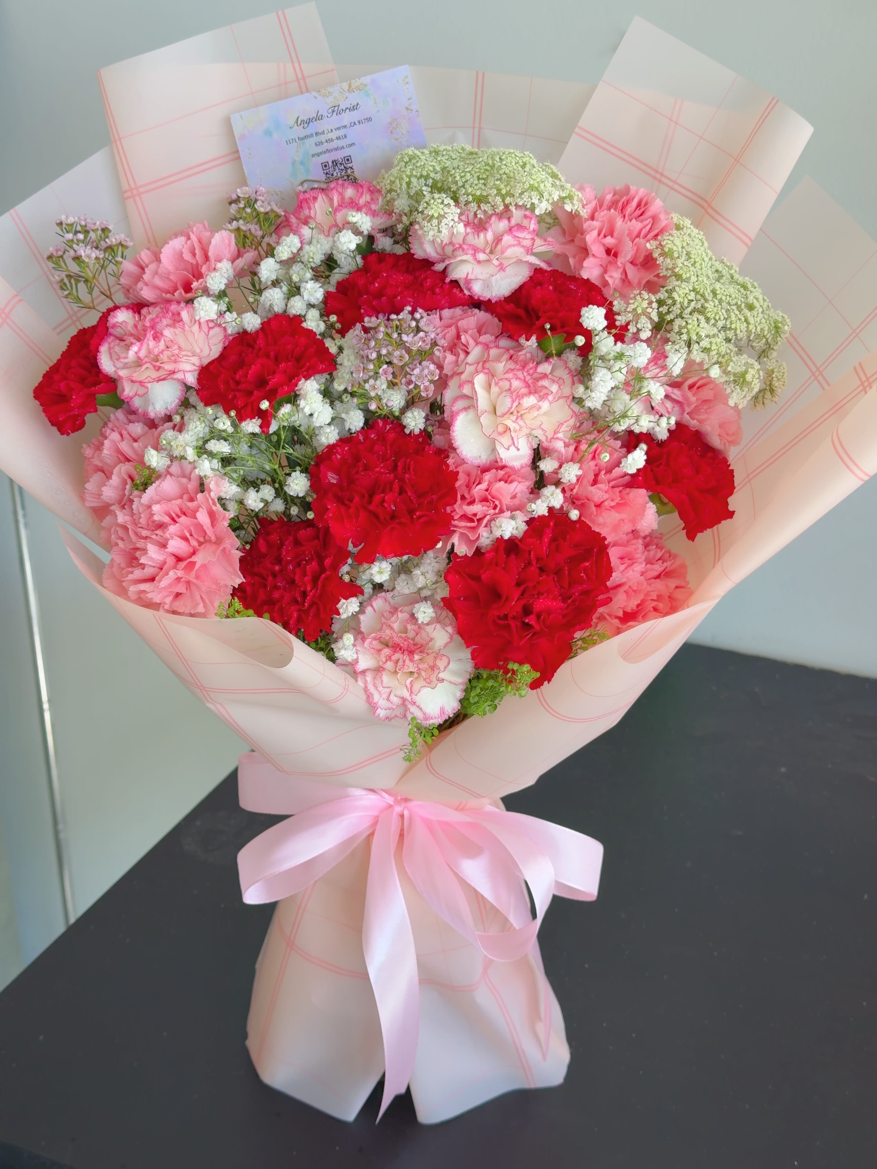 Carnation bouquet  - The product contains red and pink carnations with green leafy flowers and is packaged in wrapping paper 