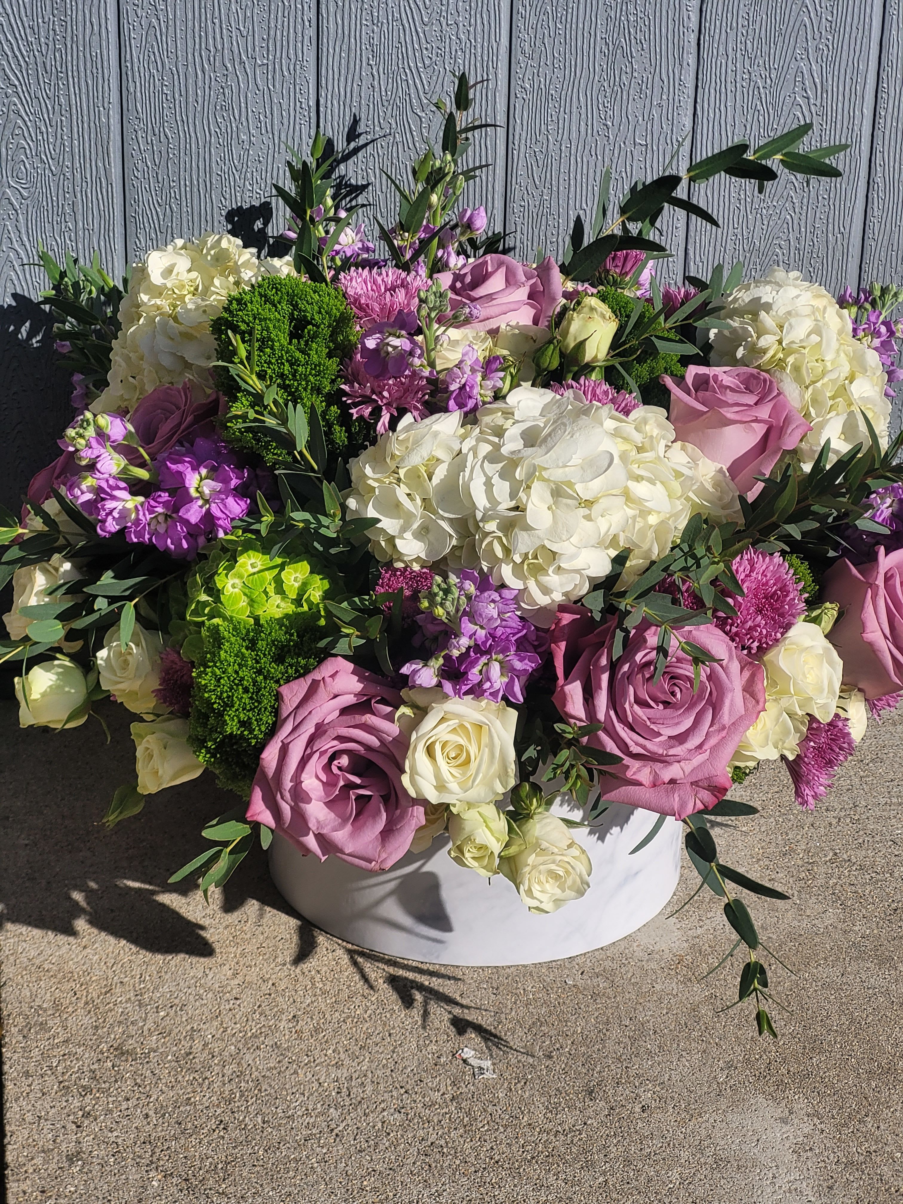 Lavender Luxe - A refined arrangement of purple and white blooms with fresh greenery, creating a soft and elegant contrast. Styled in a white hat box for a clean, modern presentation.