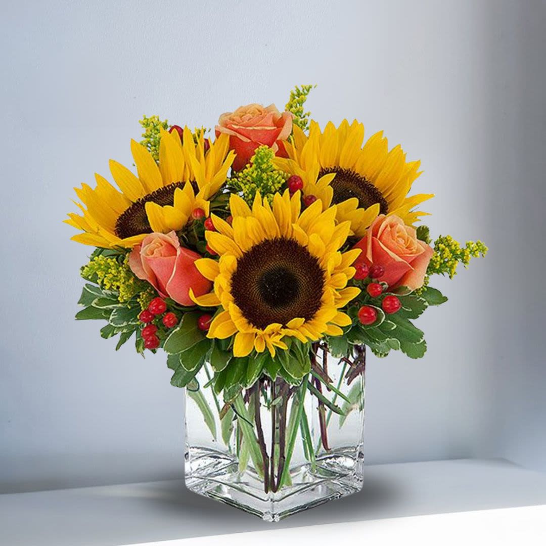 Sunflowers with Regular Roses - Brighten up a table, send get well wishes, or simply sprinkle sunshine on someone's day with this summer flower arrangement. Bold sunflowers with regular orange roses are arranged in a square 6" vase. Sunflowers steal the show in this simple arrangement. Also featured: orange hypericum, salal leaves and a curly willow inside the glass bubble bowl. Orientation: All-Around