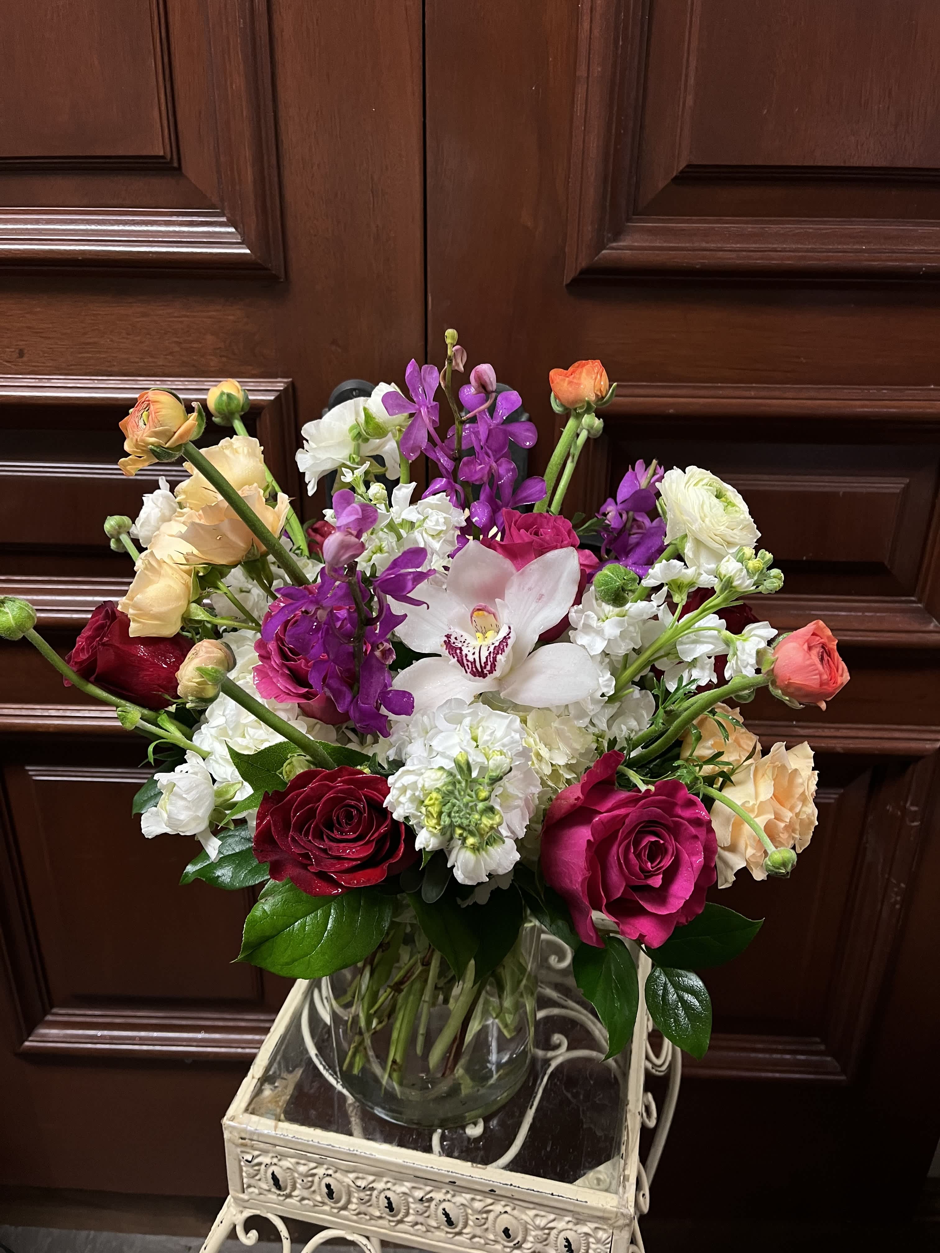 Peachy Paradise - Recipe: Seasonal Ranuculus, Tropical Orchids, Roses, Spray Roses, Stock, and more in a round, crystal vase. Availability: Seasonal Design View: All facing View Photo shown: Standard