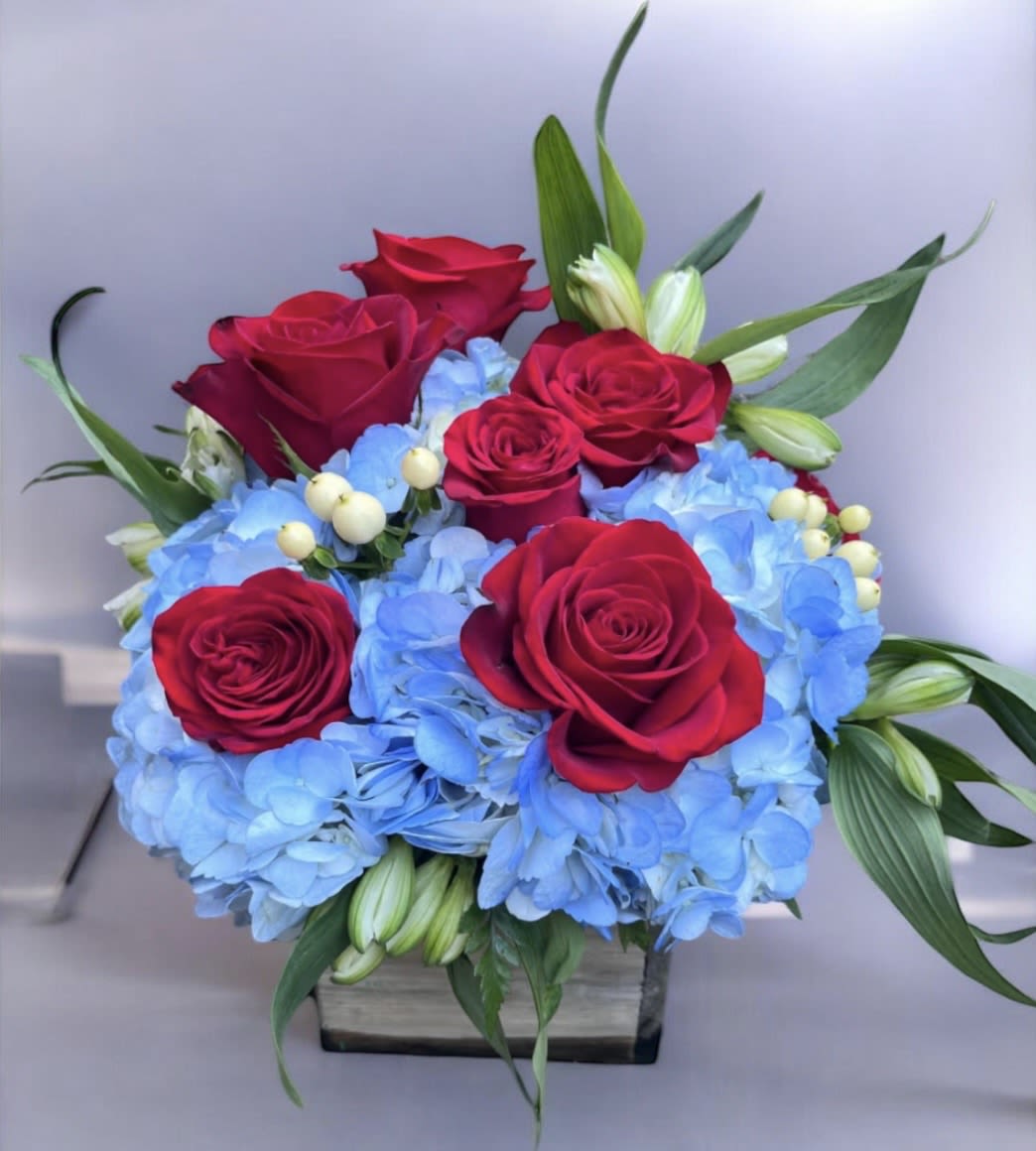 USA - This arrangement has red roses, blue hydrangeas, white alstroemeria and white Hypericum in a wooden container. 