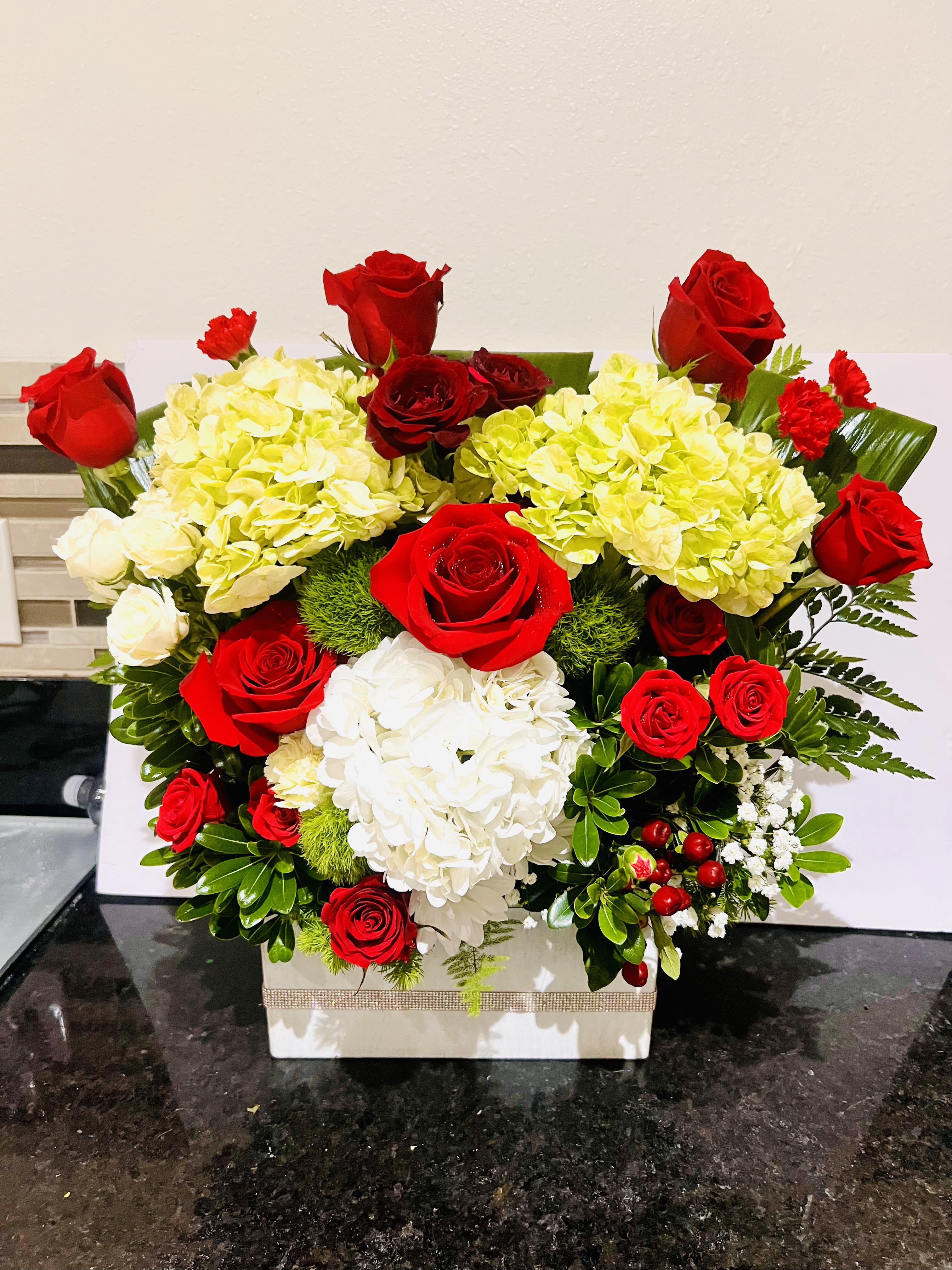 Scarlet Symphony - Eye catching floral arrangement featuring lush, velvety roses in shades of red,paired with delicate greenery and soft filler berries. The roses take center stage, symbolizing love and elegance, while accents of aspidistra add a touch of freshness and charm. Perfect for romantic occasions, celebrations, or as a timeless statement of beauty.  For same day delivery and Free Delivery Options Call 832-973-1376. 