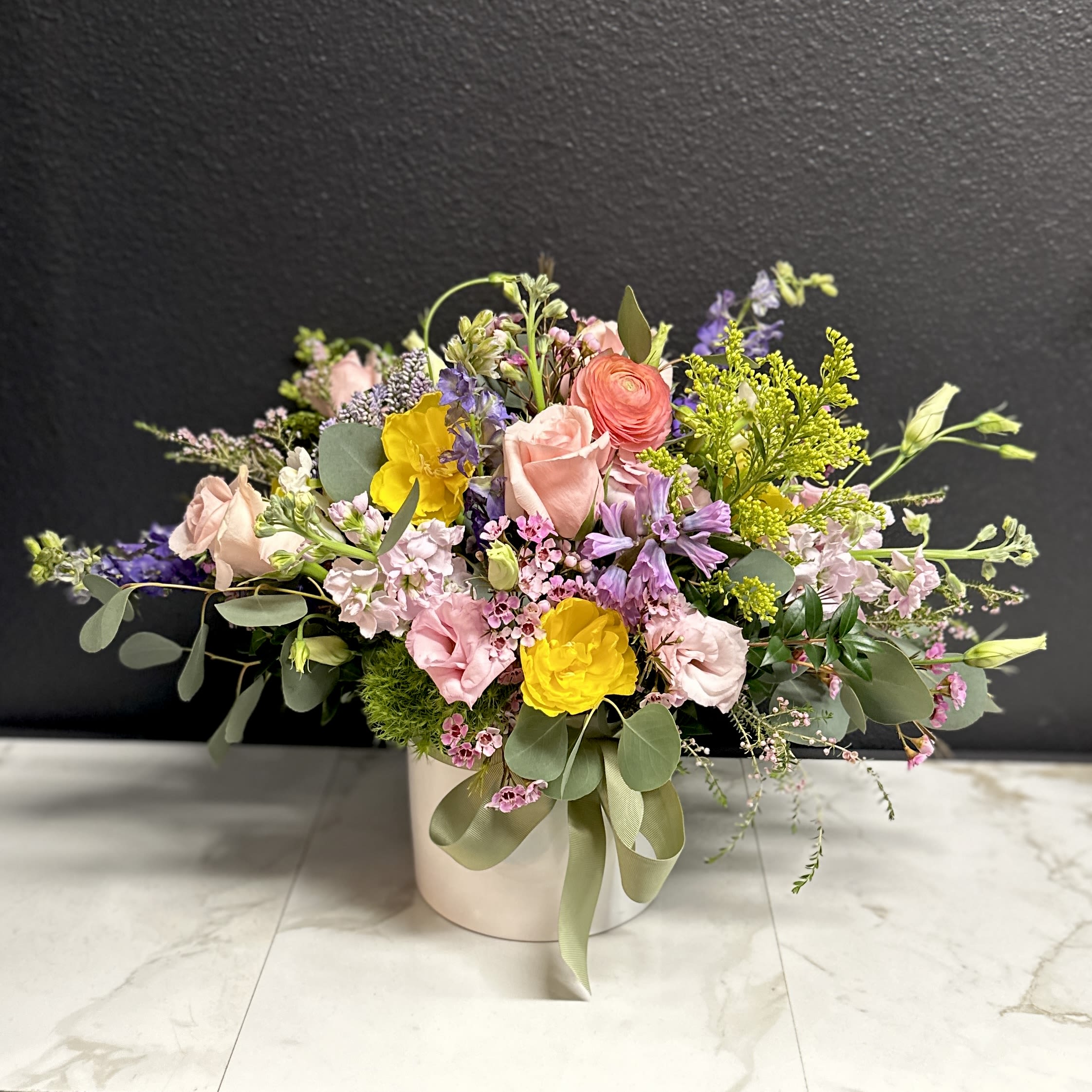 Soft Spring Meadow - A loose and airy garden mix in soft Spring pastels. Delivered in a white ceramic vase. Overall design is approximately 15"H x 22"W x 15"D.  While the varieties may vary the overall look will be of similar style &amp; quality. 