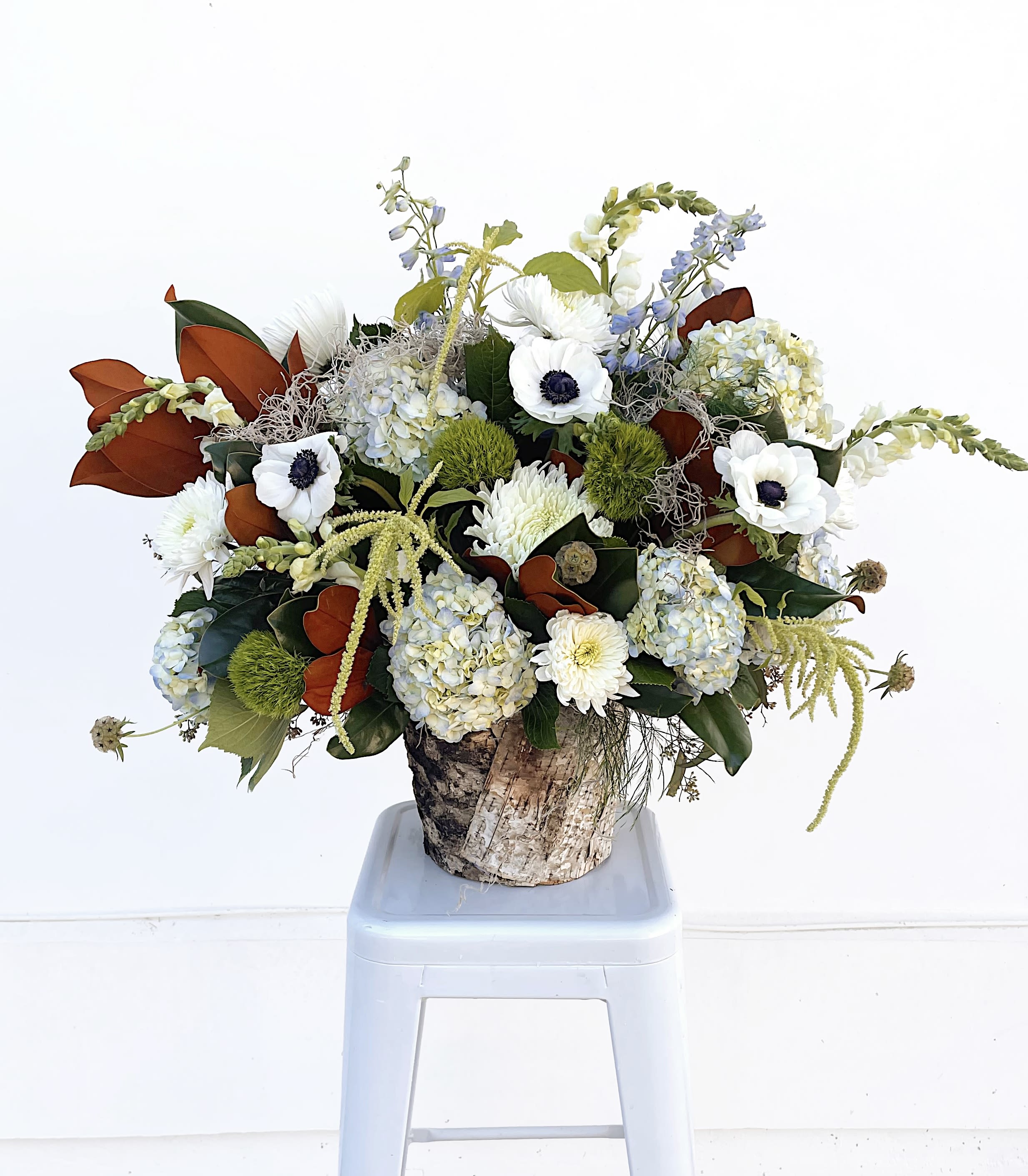 Whispering Woodland - Woodland Awakening captures the serene beauty of a forest coming to life in early spring, featuring fluffy hydrangeas, lush magnolia leaves, cascading amaranthus, delicate anemones, and elegant snapdragons. This organic, textured blend of seasonal greenery and soft, romantic blooms creates the perfect centerpiece to brighten your spring parties or freshen up your home decor.  ***Smaller size option available by phone***