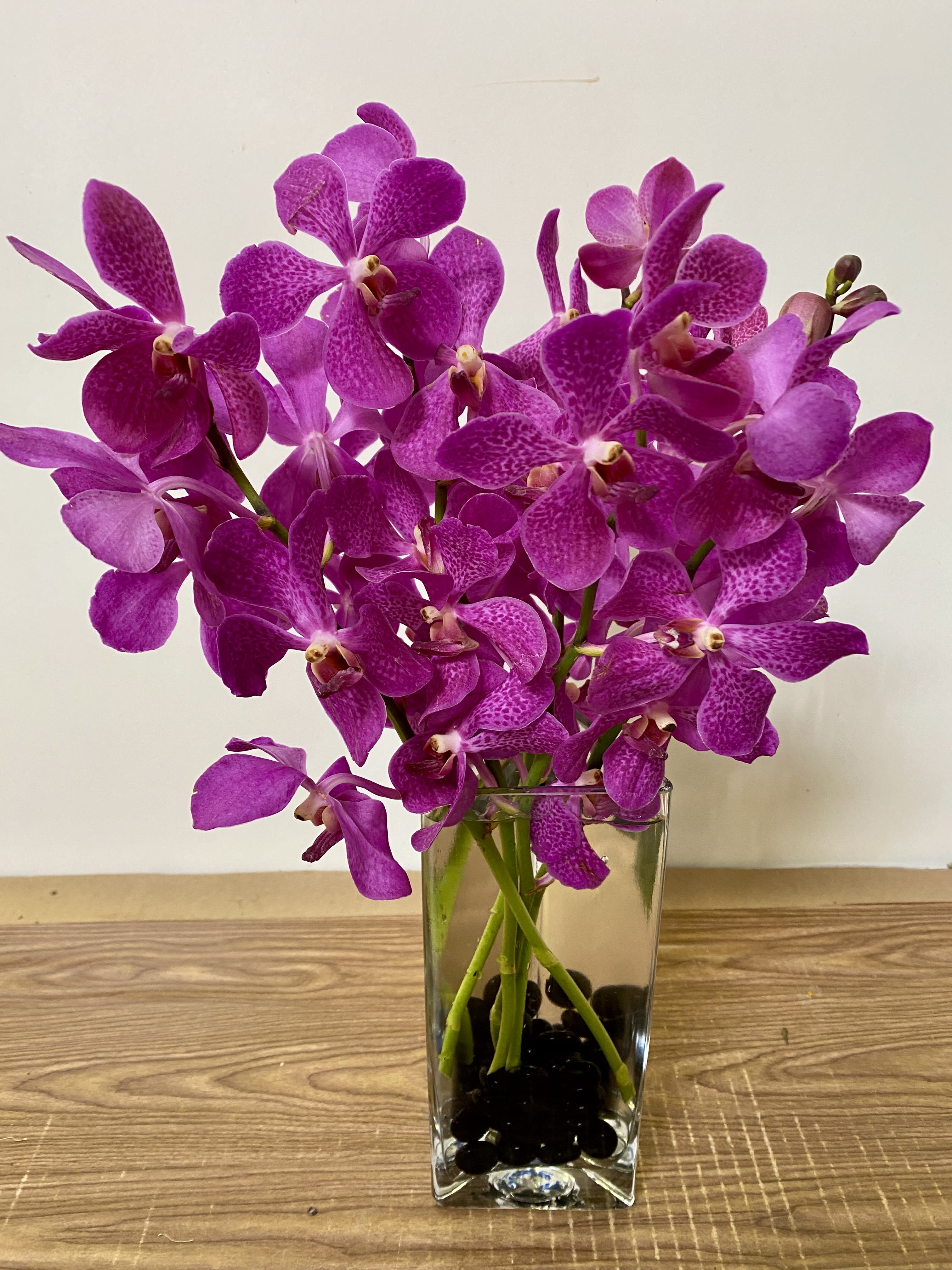 Before Midnight - clear glass vase with a black stones and 5 orchids. Orchids can be white, peach, pink or purple  