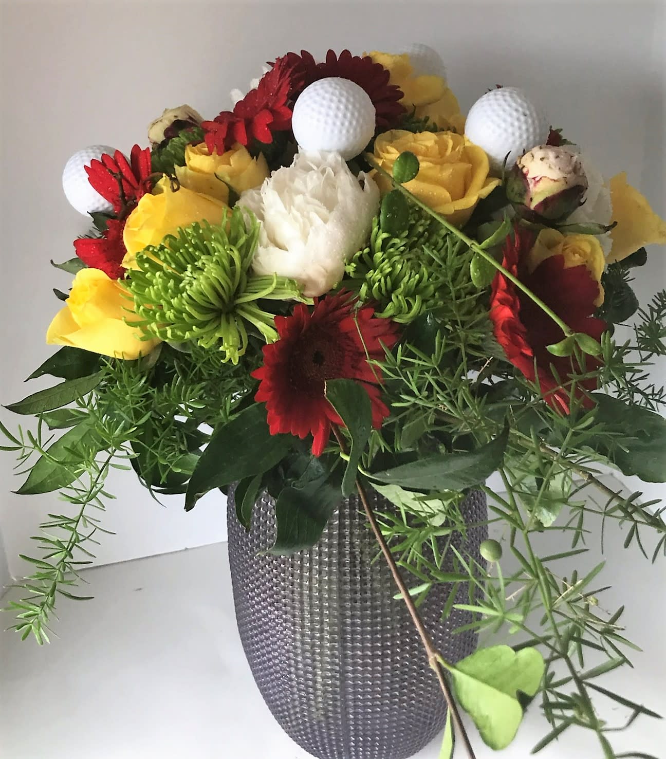 Golfers Delight - A sure win for any golf lover. Created in a custom vase. Filled with seasonal blooms and greens and topped off with golf balls.