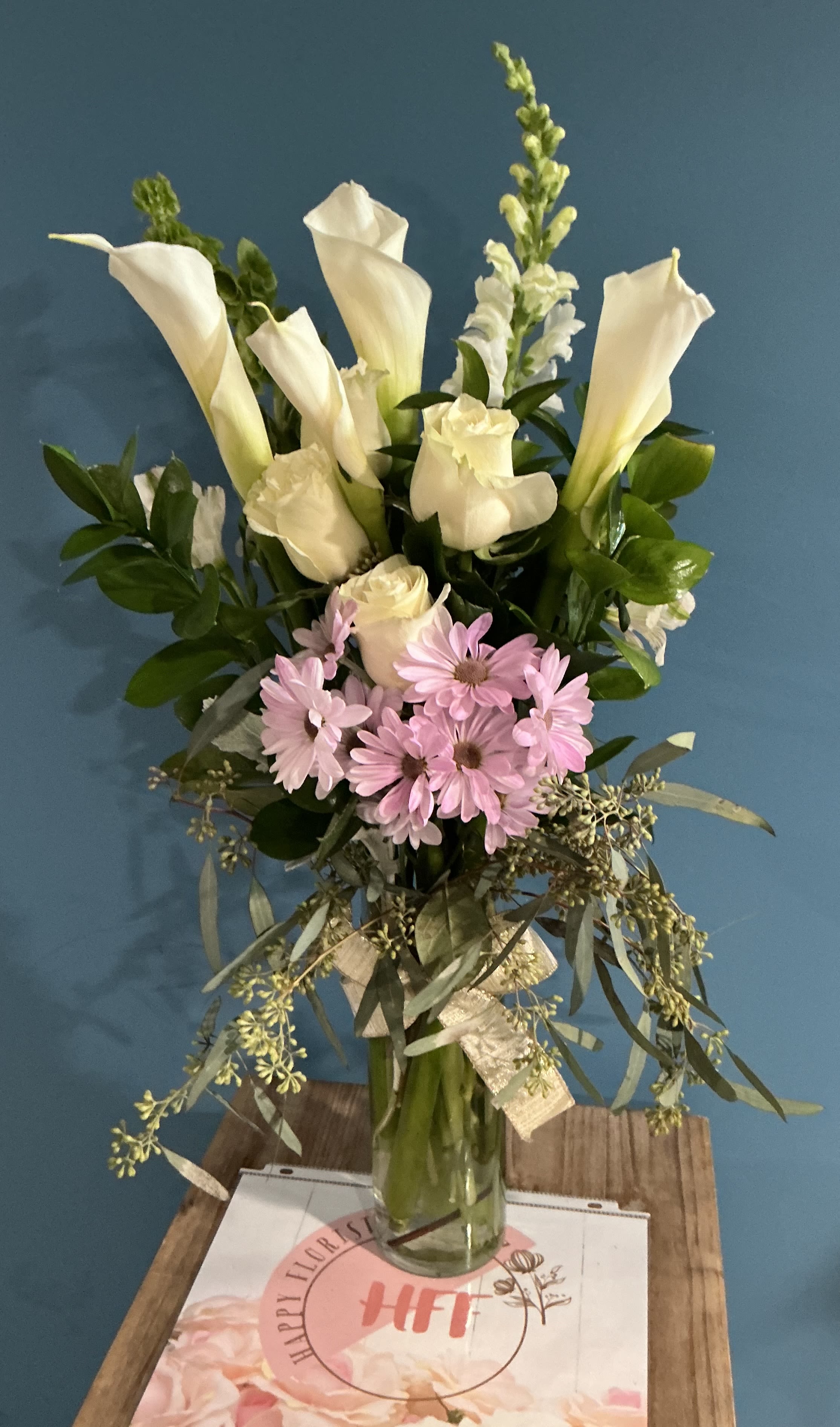 Calla Lilies  - This floral arrangement with white calla lilies,  white roses, snapdragon, bell of Ireland  Black eyes daisy and greenery gives support any special occasion  Cylinder vase 25H 18W