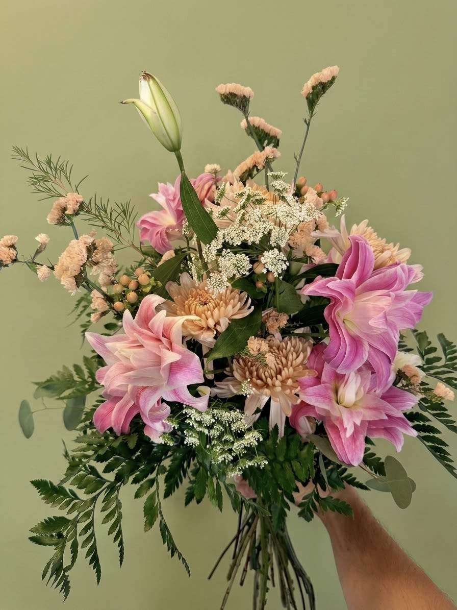 Lowcountry Lily  - An exploration of Southern poise and layered texture. This signature arrangement features the dramatic, ruffled petals of Double Oriental Lilies complemented by the soft, architectural form of Peach Cremones. Accented with the delicate, lace-like mist of Queen Anne’s Lace and the warm glow of Peach Hypericum berries, it is grounded in a lush, custom mix of seasonal greenery. A timeless centerpiece designed to elevate any setting or occasion.