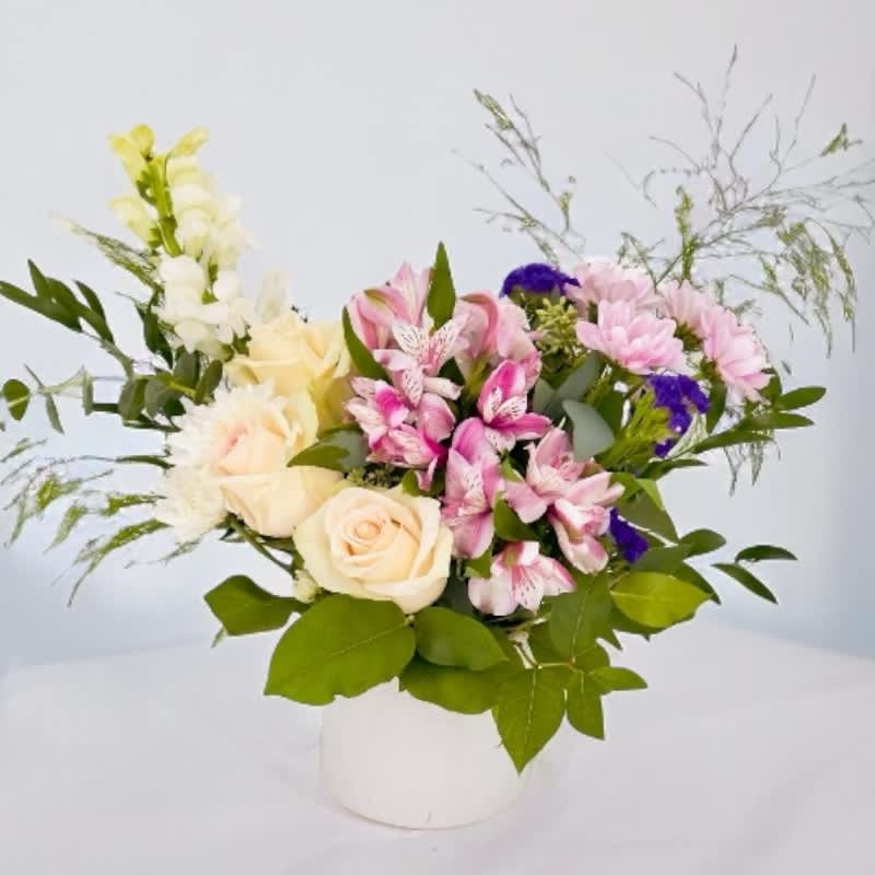 Brigid's Celtic Harmony #21 - "Brigid's Celtic Harmony" is a captivating flower arrangement inspired by Brigid, the revered Irish goddess associated with healing, poetry, and the hearth. It features Perla roses, Lavender pom, White poms, Purple statice, White snapdragons, Purple-white alstroemeria, and a blend of foliage, including Seeded eucalyptus, Tree fern, Italian ruscus, Salal, and Baby blue eucalyptus. "Brigid's Celtic Harmony" pays homage to the goddess's versatile powers and deep-rooted Celtic traditions. This arrangement is a perfect gift to celebrate the Celtic spirit, connect with the hearth, or convey love and creativity in a poetic and healing manner.
